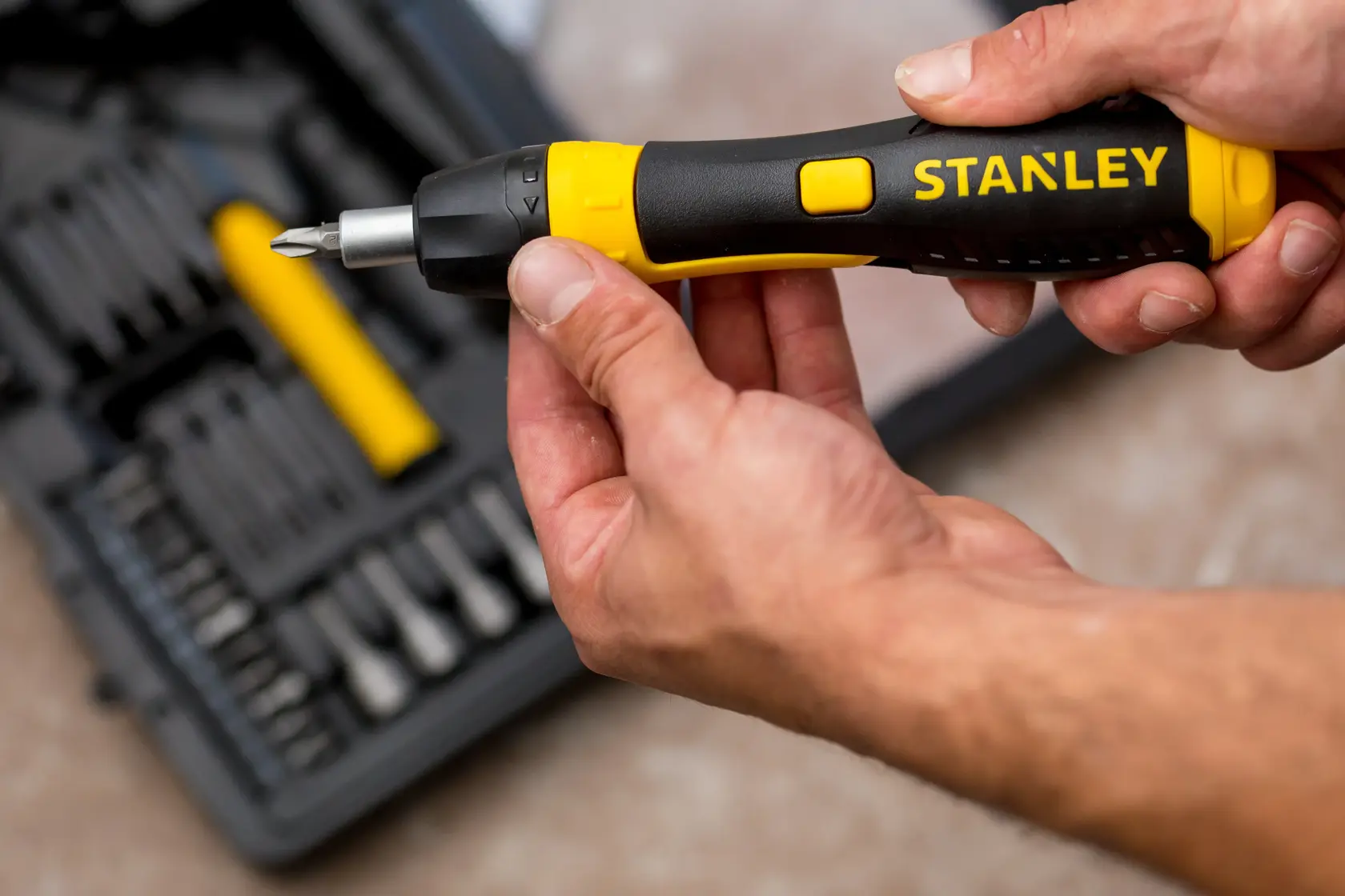 Cacciavite a cricchetto STANLEY 0-63-038 con manico nero e giallo tenuto in mano, kit di attrezzi sullo sfondo.