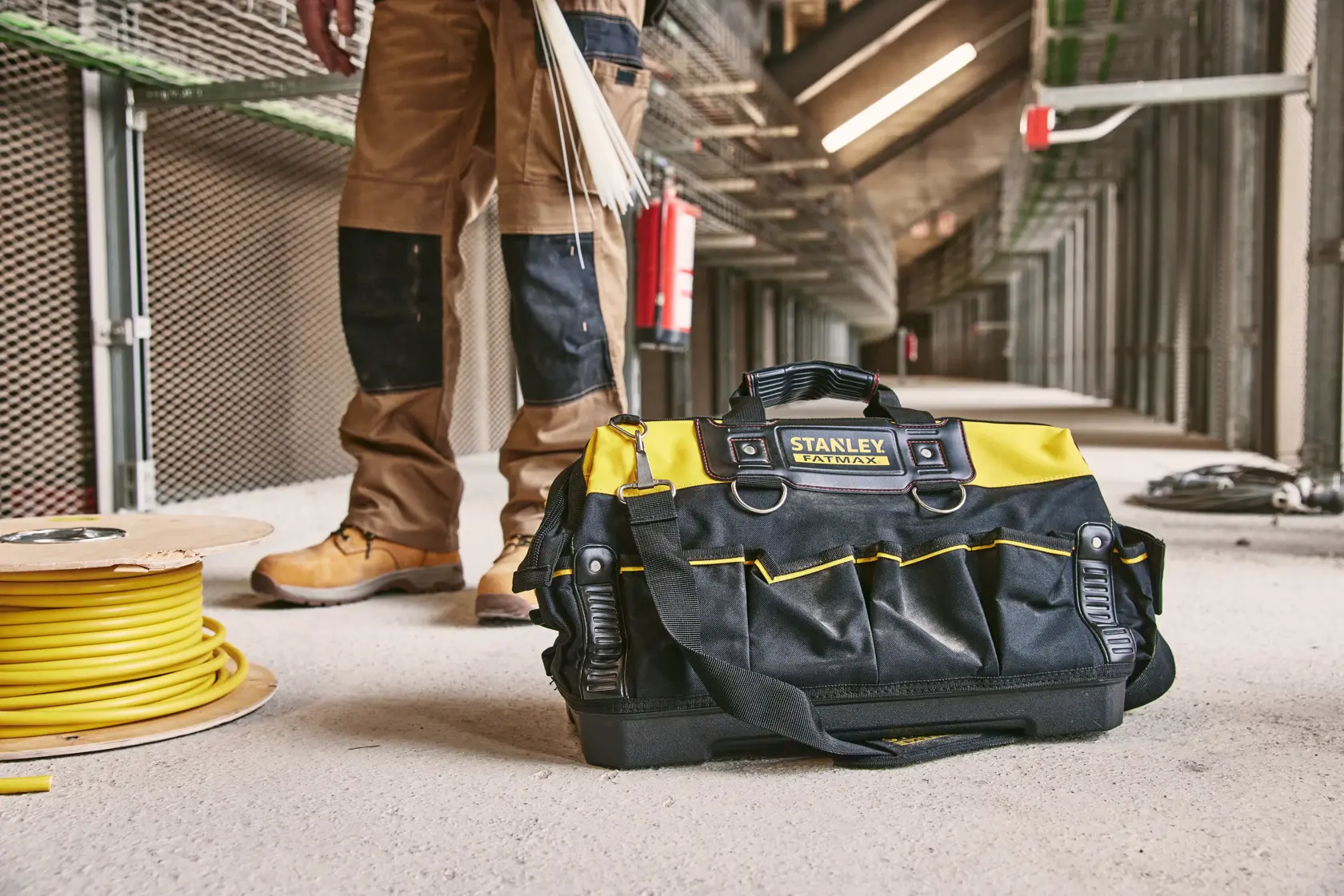 Borsa porta attrezzi STANLEY 1-93-950 nera e gialla con manici, su un cantiere vicino a bobina di cavo.