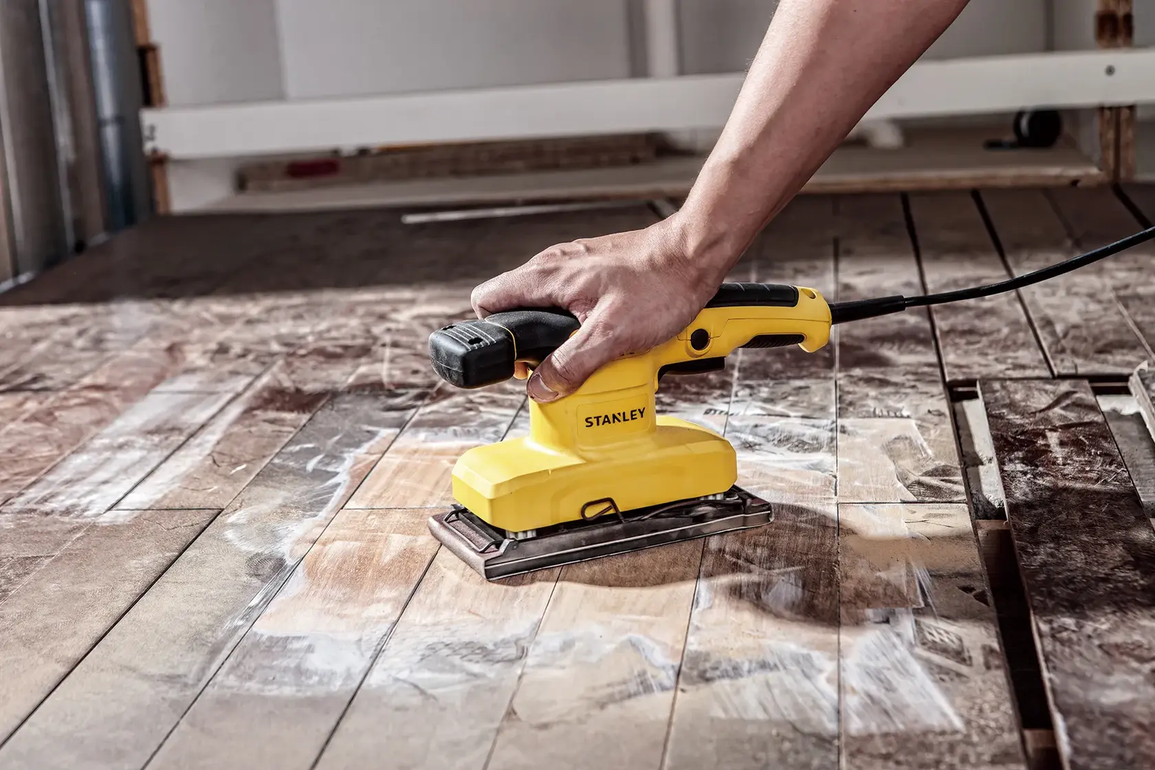Levigatrice orbitale STANLEY SS28-AR in uso su pavimento in legno, vista laterale, design giallo e nero.