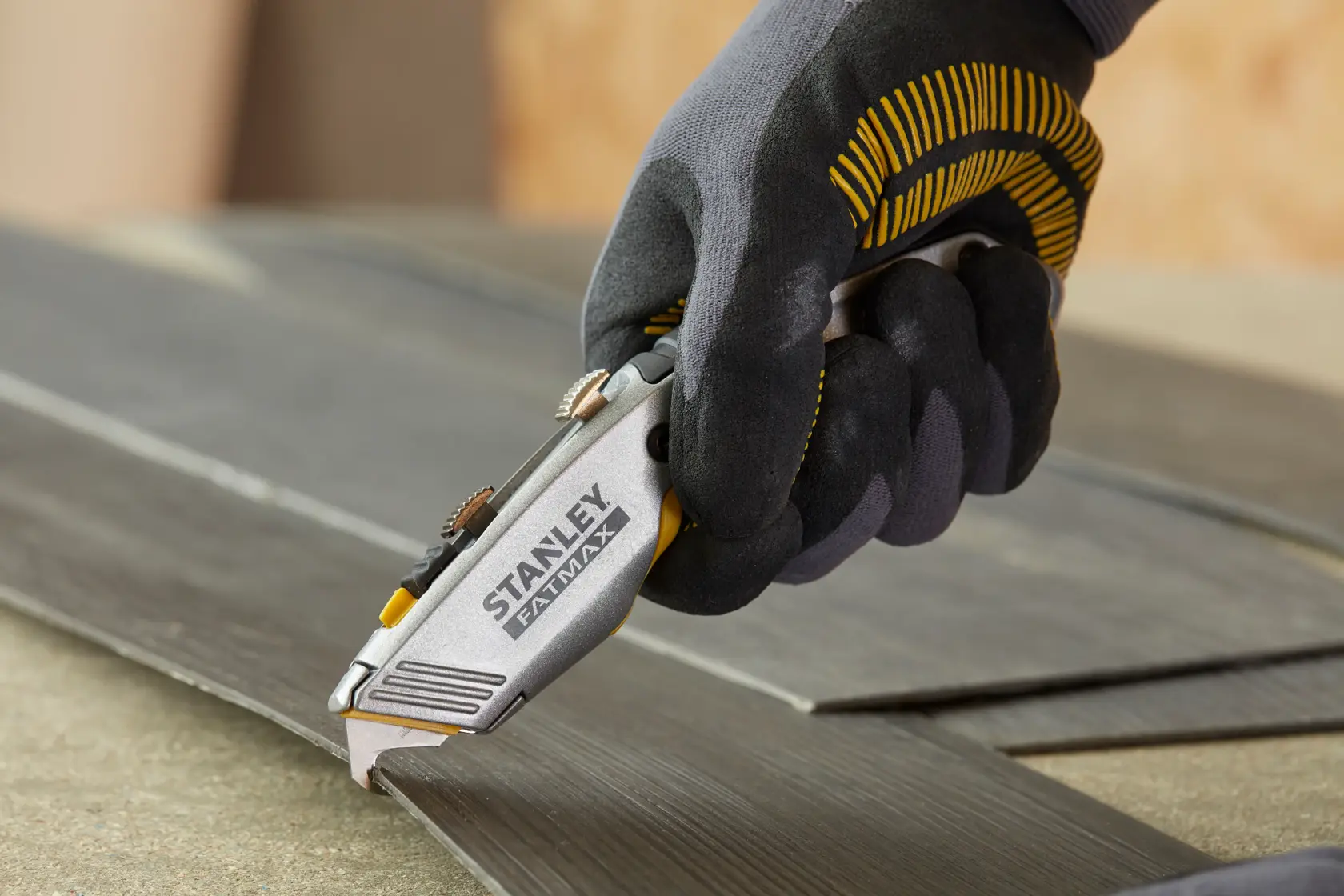 Coltello Stanley 0-10-789 tenuto con guanto taglia pavimento laminato scuro.