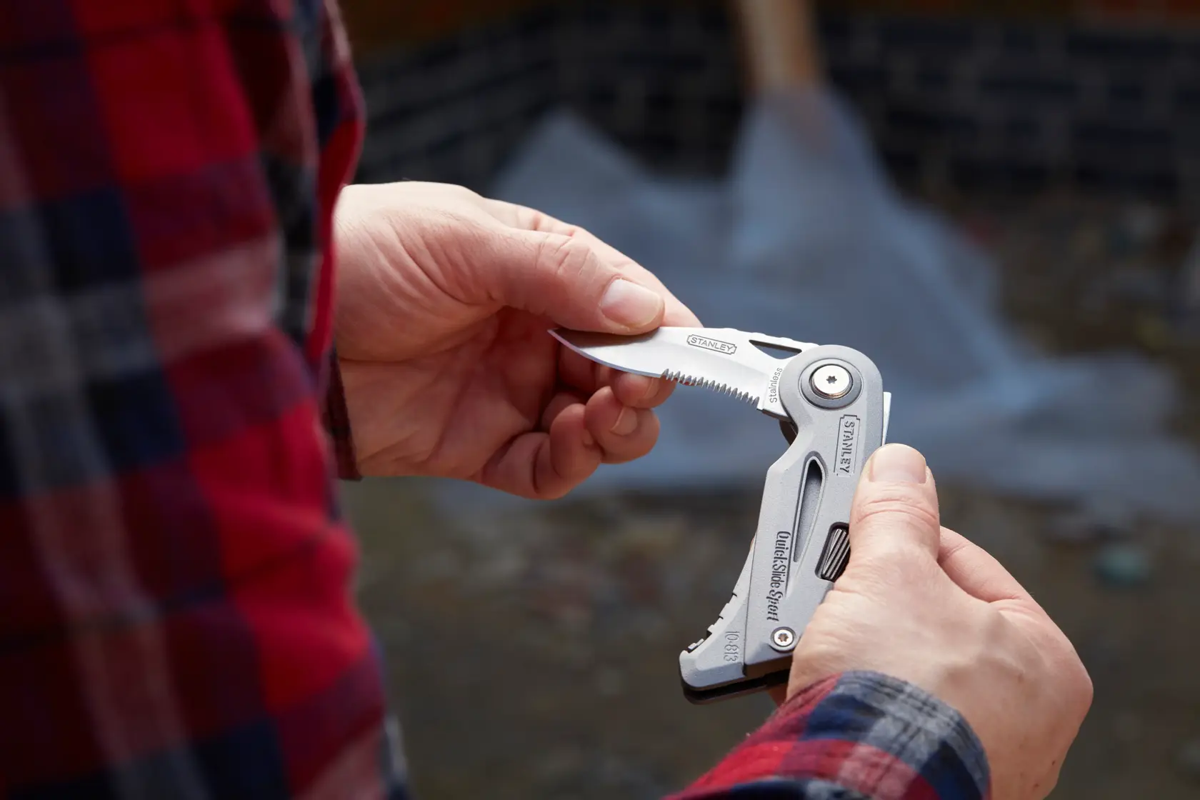 Fotografia del coltello multitool STANLEY 0-10-813 tenuto all'aperto, parzialmente aperto con lama seghettata visibile.