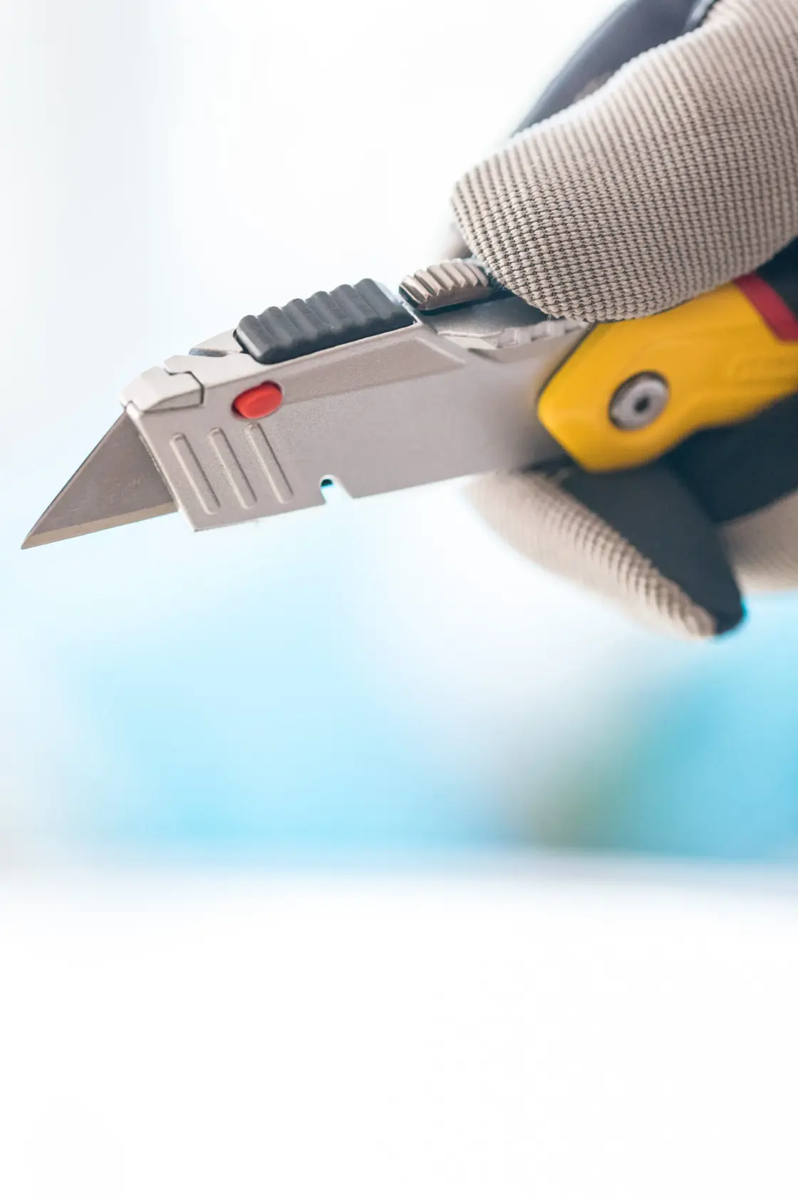 Coltello universale STANLEY 0-10-825 con lama retrattile, tenuto in mano guantata, primo piano.