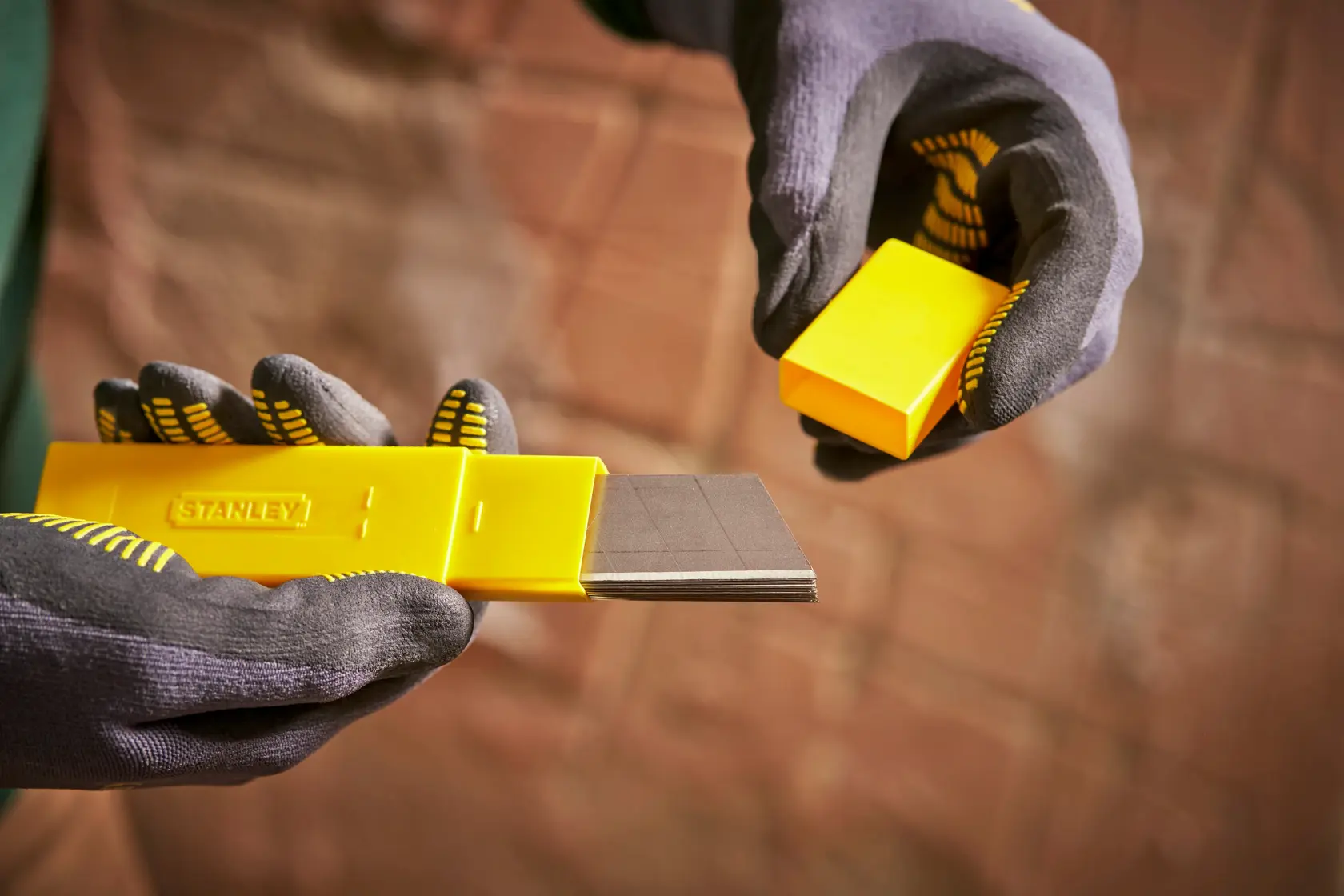 Dispenser di lame giallo STANLEY 0-11-325 tenuto da mani guantate, mostra diverse lame.