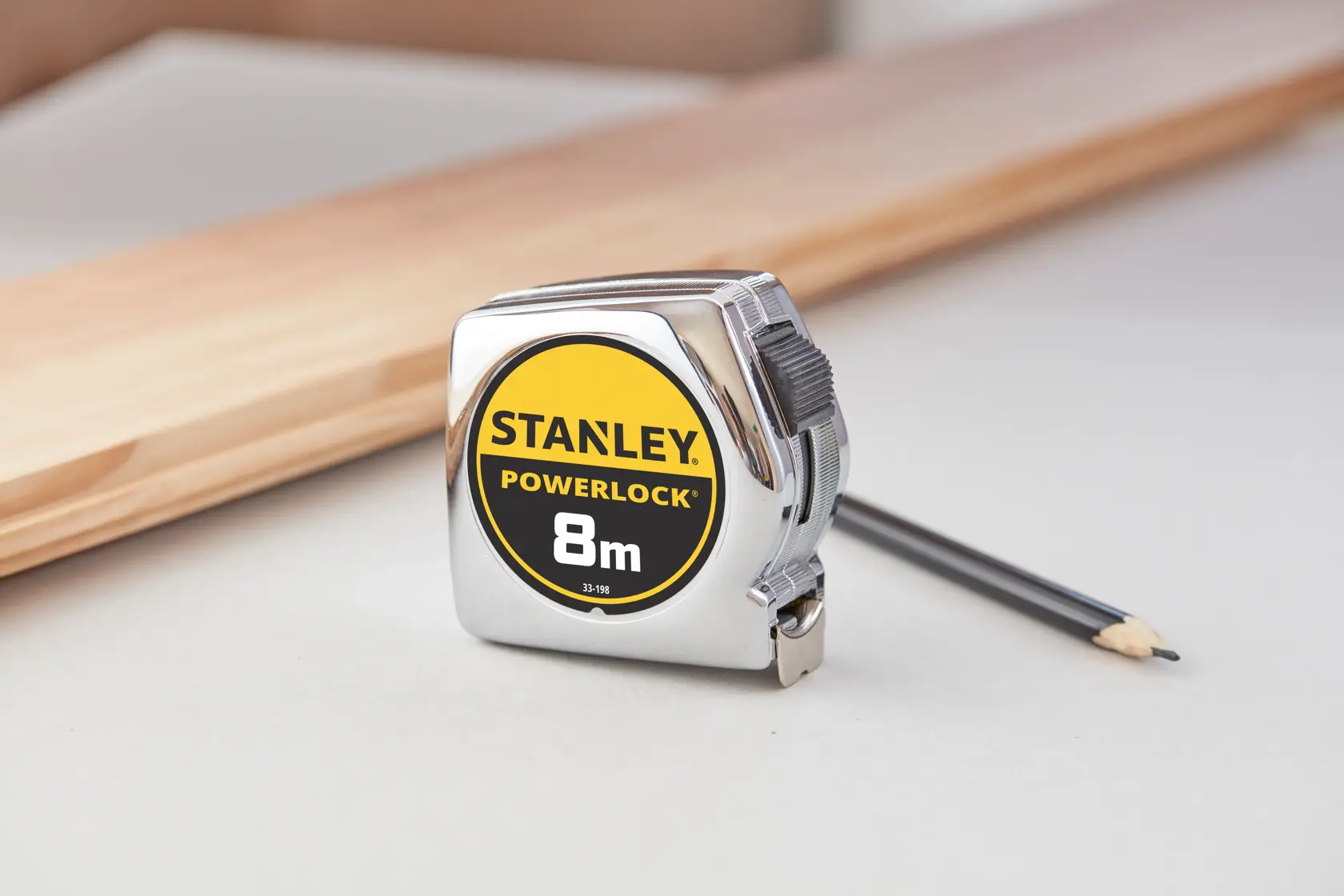 STANLEY 0-33-198 PowerLock metro a nastro 8m con custodia cromata, su tavolo con matita e legno.