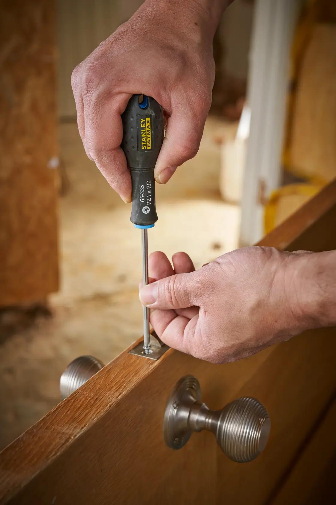 Foto del cacciavite STANLEY 0-65-335 utilizzato per stringere una vite su cerniera metallica di porta in legno.