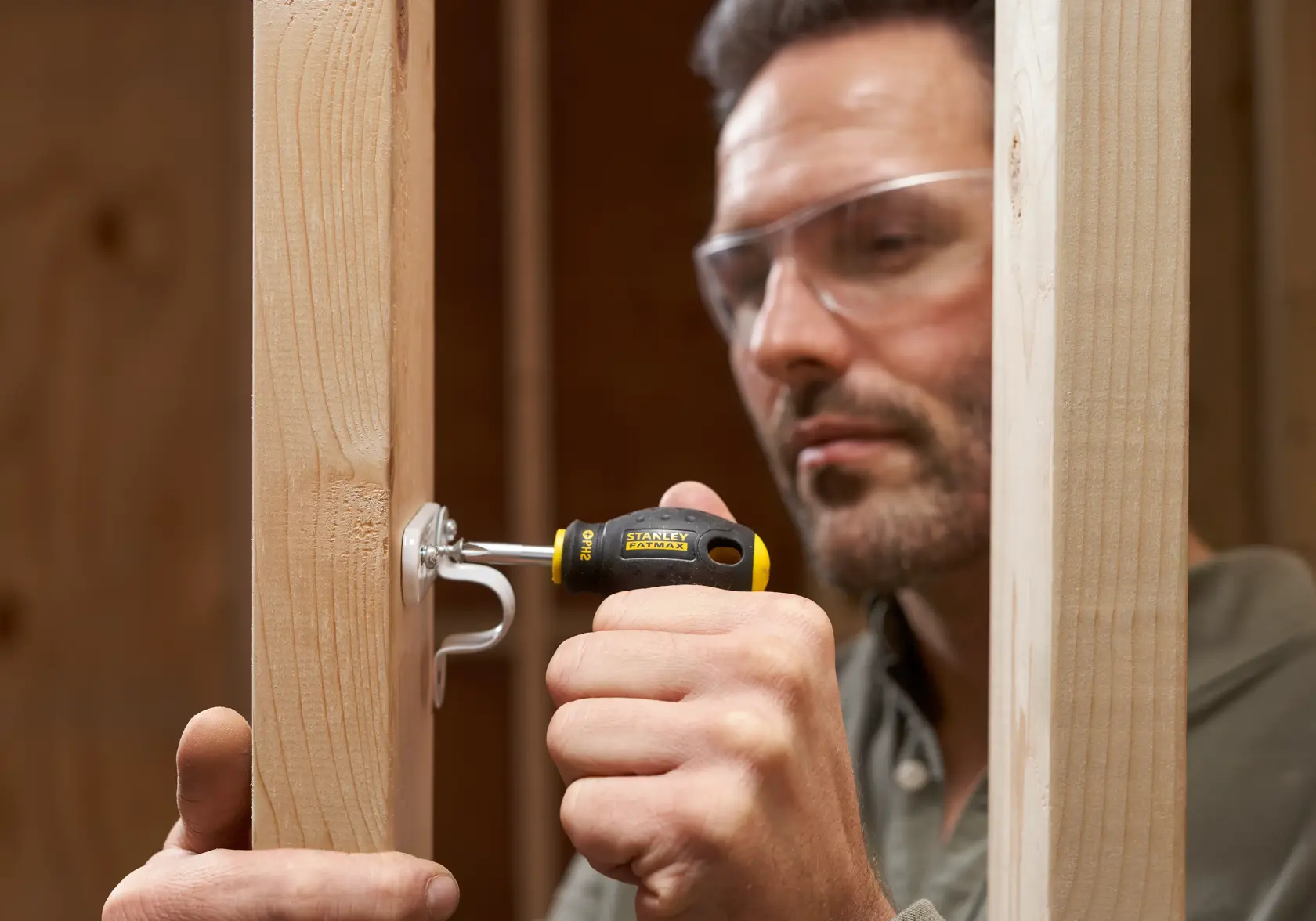 STANLEY 0-65-407 cacciavite utilizzato per fissare un gancio a una trave di legno in un contesto di costruzione.