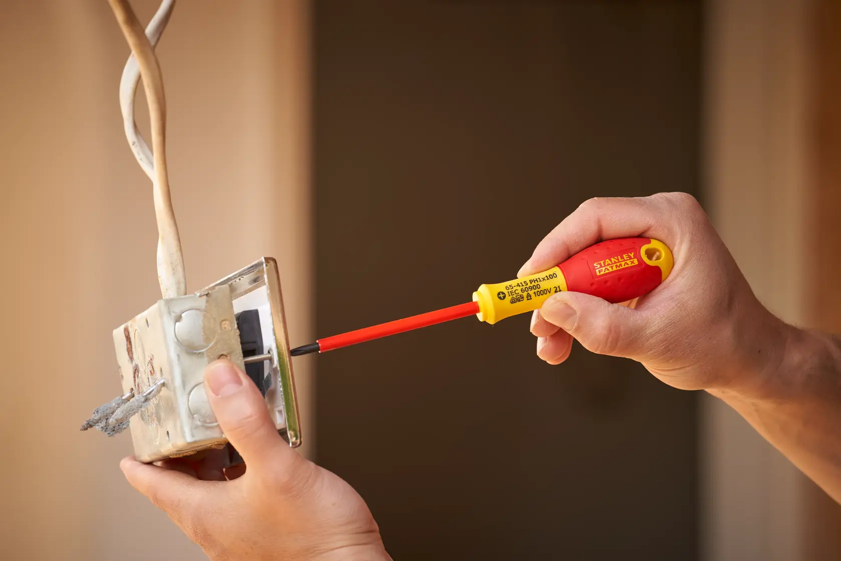 STANLEY 0-65-415 cacciavite isolato con manico rosso e giallo utilizzato per lavori elettrici su un interruttore a parete.