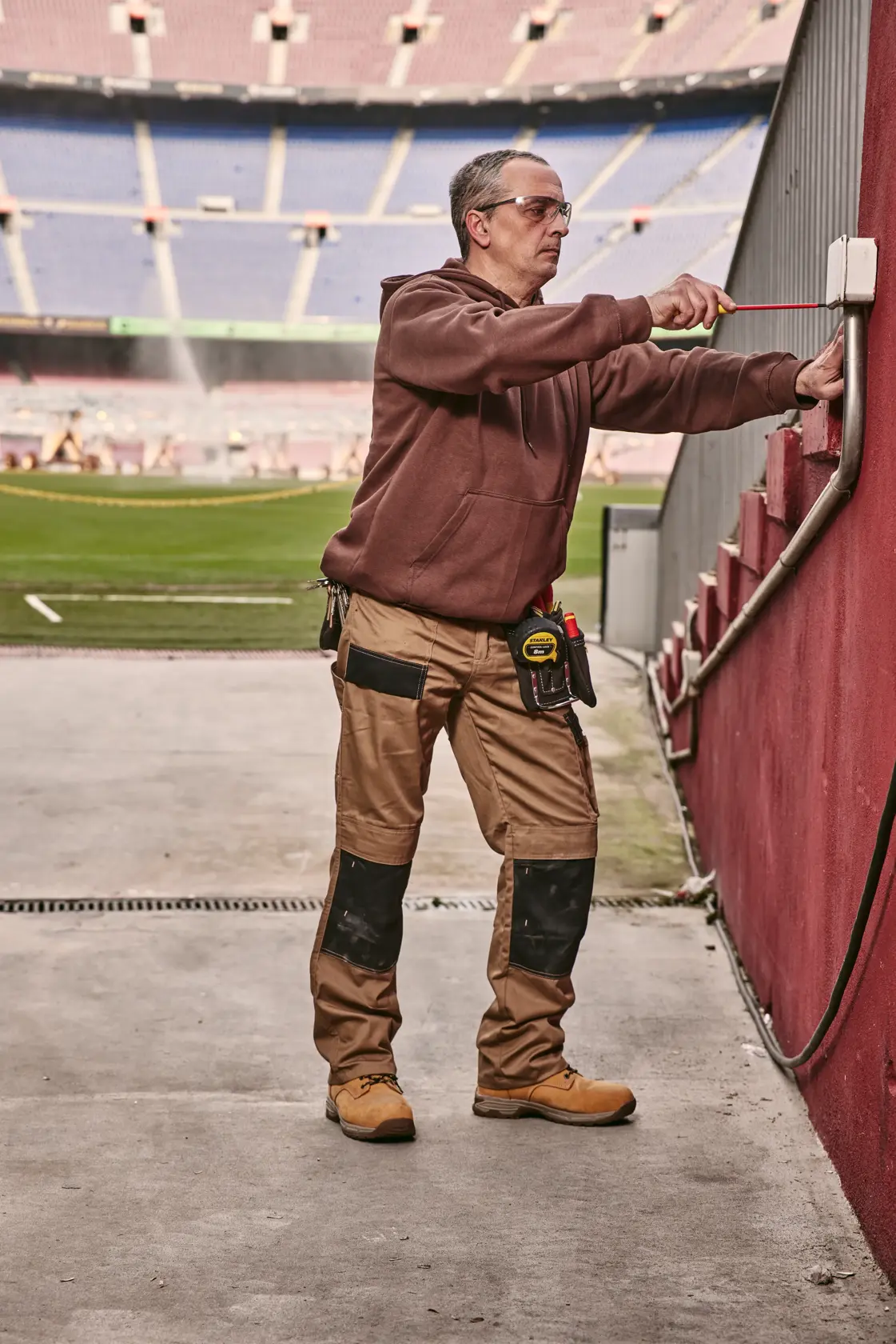 STANLEY 0-65-443 cacciavite usato da un operatore per regolare una scatola elettrica esterna vicino a un campo da stadio.