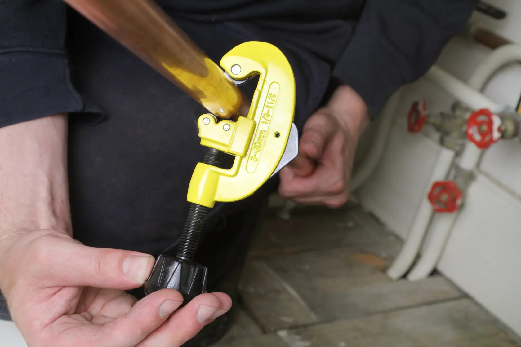 Tagliatubi STANLEY 0-70-448 in uso, corpo giallo su tubo di rame, mani che regolano l’attrezzo, contesto idraulico.
