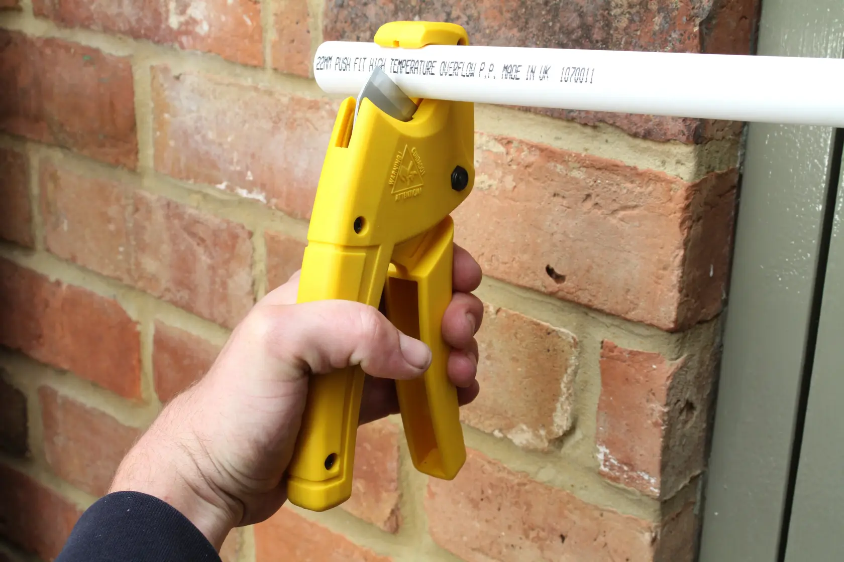 STANLEY 0-70-450 tagliatubi giallo usato per tagliare un tubo bianco vicino a un muro di mattoni, fotografia ravvicinata.