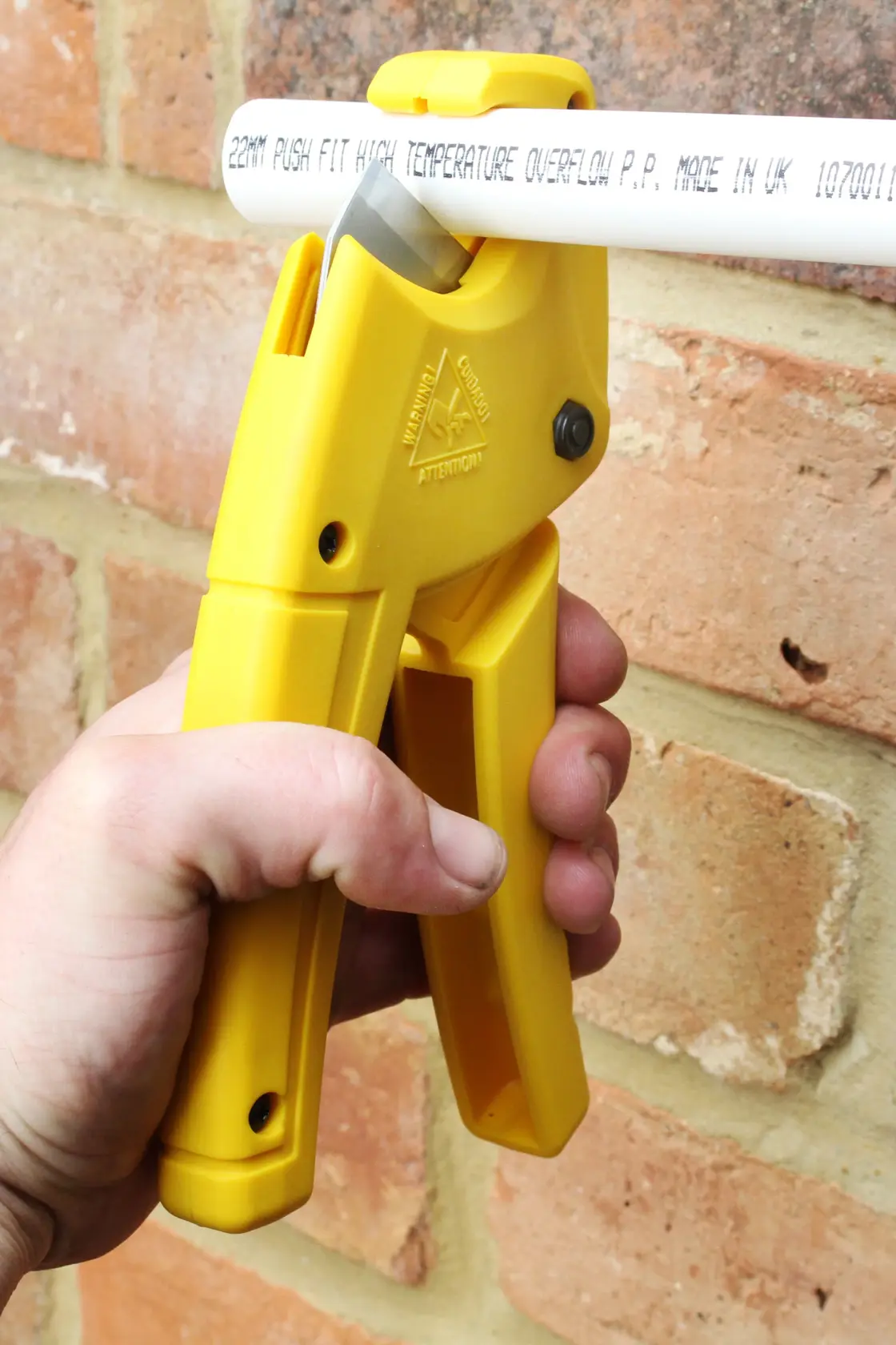 Tagliatubi in plastica giallo STANLEY 0-70-450 tenuto in mano, taglia tubo bianco, vista ravvicinata.