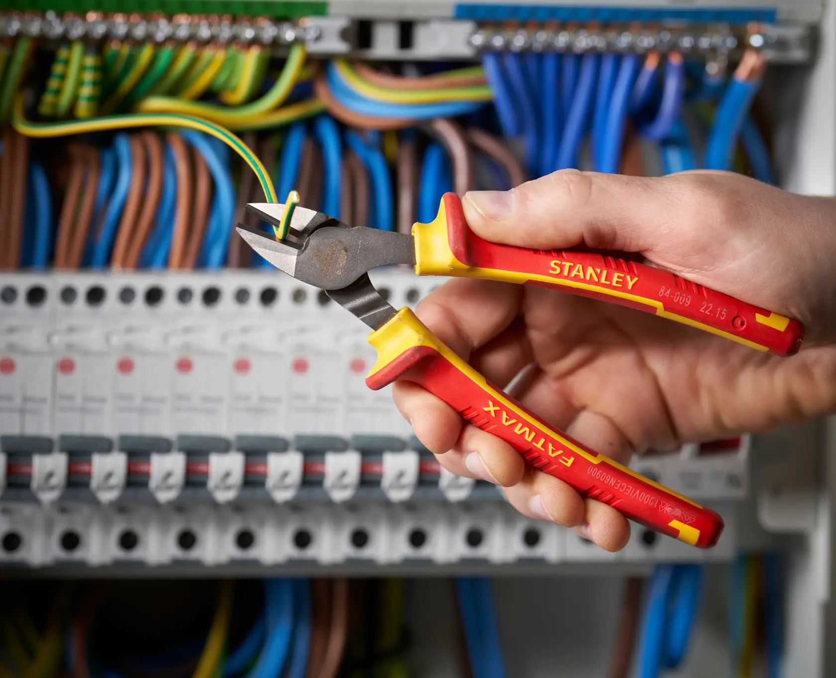 Pinza da taglio diagonale isolata STANLEY 0-84-009 tenuta in mano, taglia un filo in un quadro elettrico.