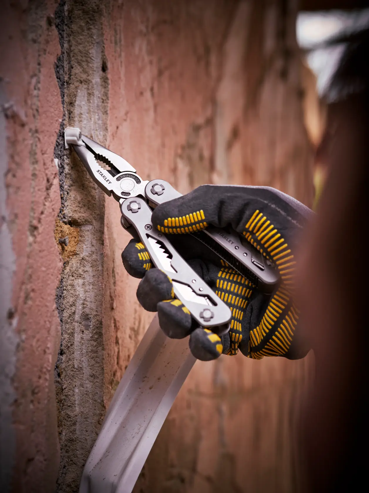 STANLEY 0-84-519 pinza multitool usata su muro di mattoni, fotografia ravvicinata di mano con guanto.
