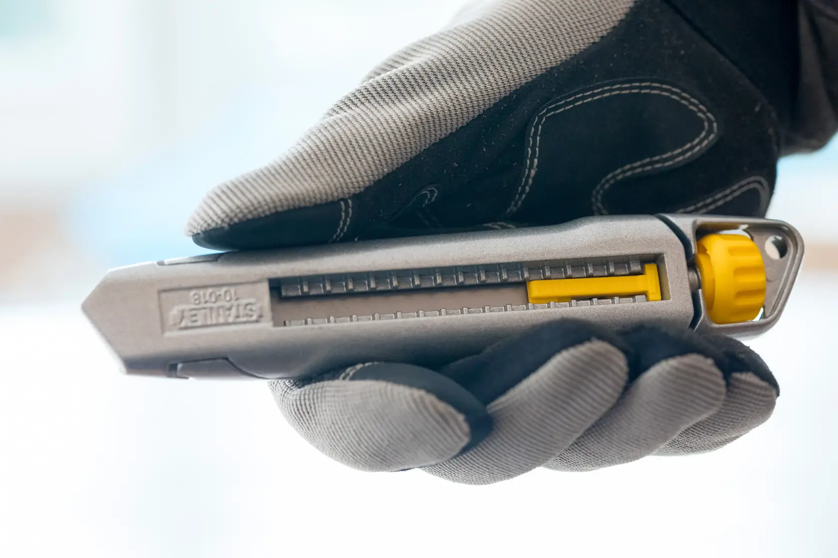 STANLEY 1-10-018 coltello universale grigio e giallo tenuto con guanto, vista laterale.