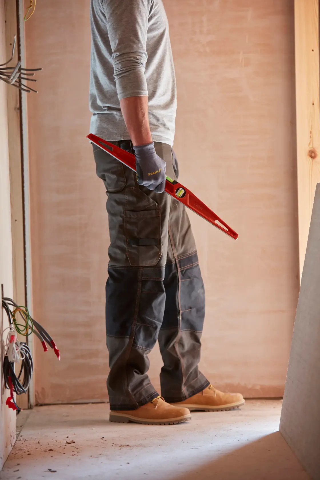 Fotografia di una persona con guanti da lavoro che tiene un livello STANLEY 1-42-314 in un cantiere.