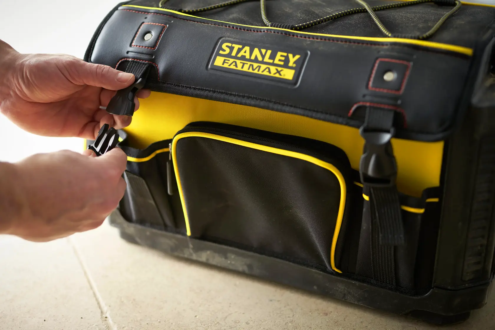 Borsa attrezzi STANLEY 1-79-213, nero e giallo, vista frontale, mani allacciano la fibbia laterale.