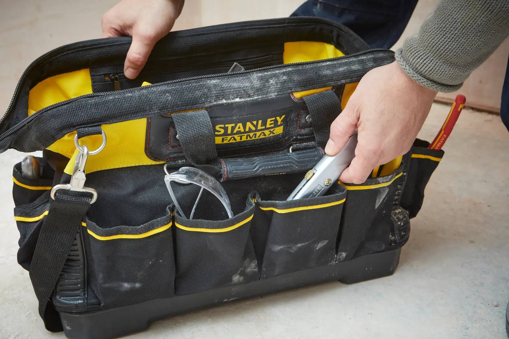 Borsa porta attrezzi STANLEY 1-93-950 gialla e nera, aperta con una mano, attrezzi e occhiali protettivi visibili.