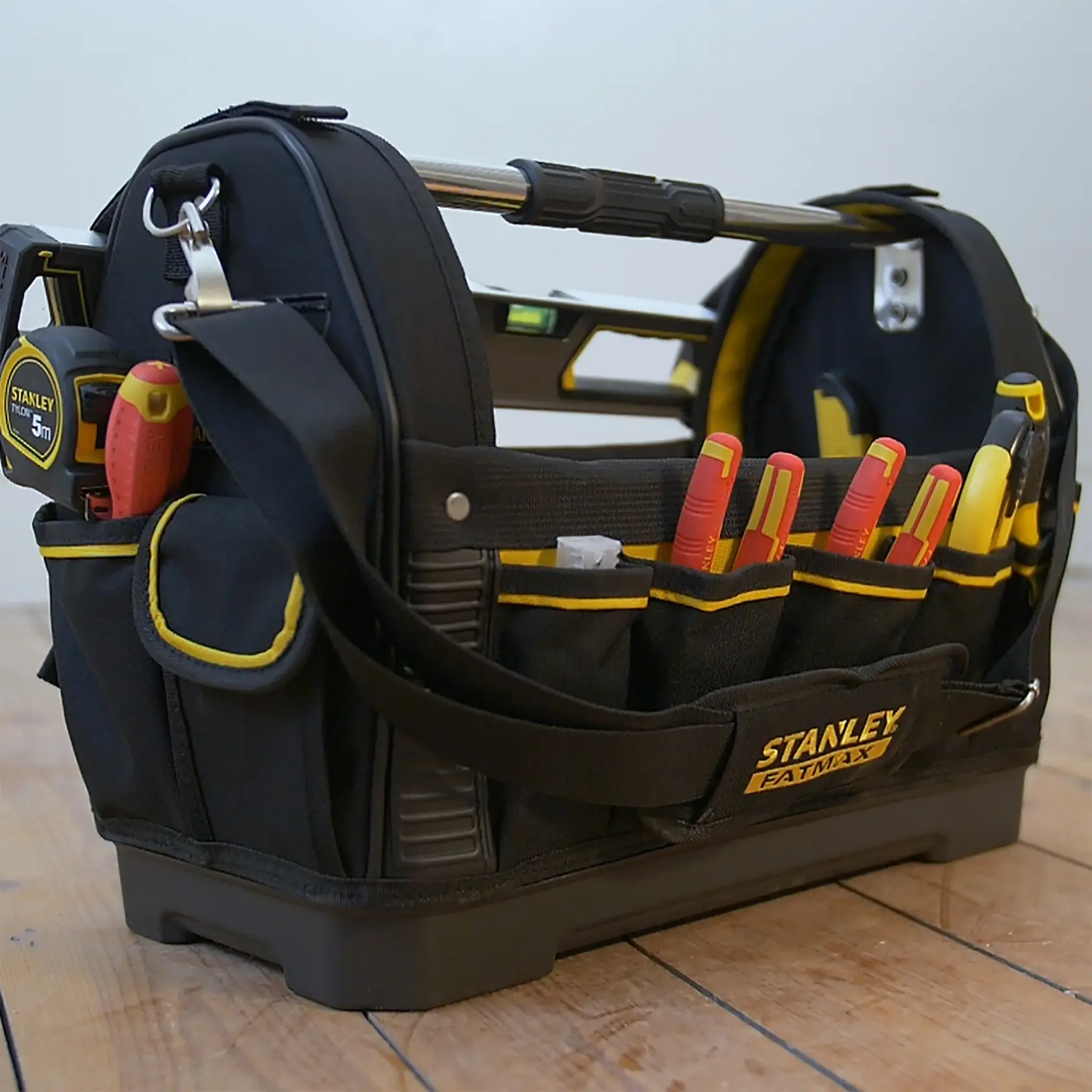 Borsa porta attrezzi STANLEY 1-93-951 FATMAX con attrezzi, vista laterale, nera e gialla su pavimento in legno.