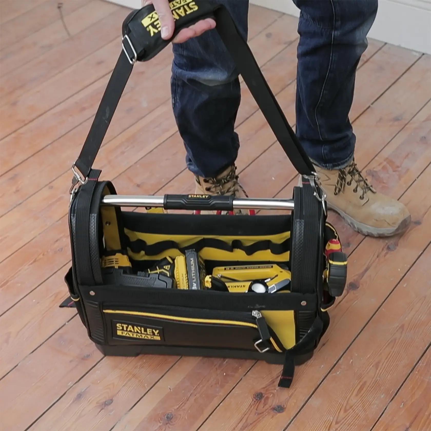 Borsa porta attrezzi STANLEY 1-93-951 con tracolla piena di attrezzi, fotografata su pavimento in legno.