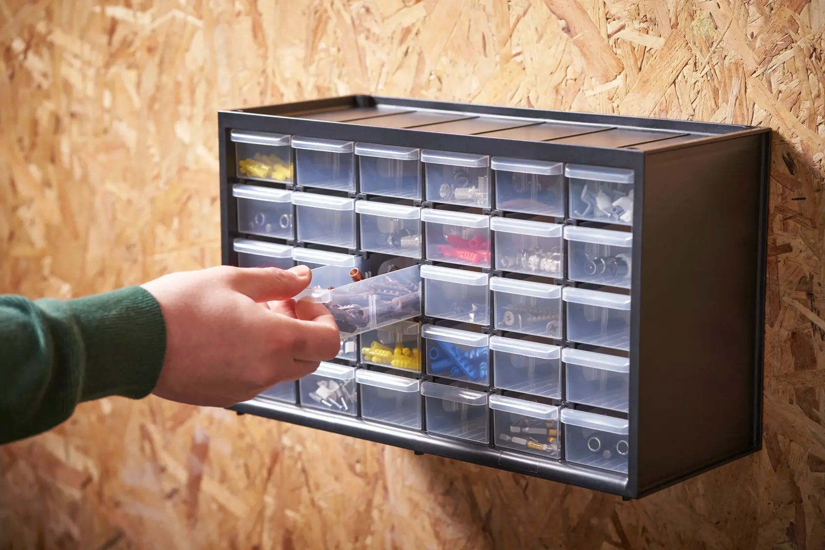 Organizer STANLEY 1-93-980 con cassetti trasparenti montato a parete, mano accede al contenuto.