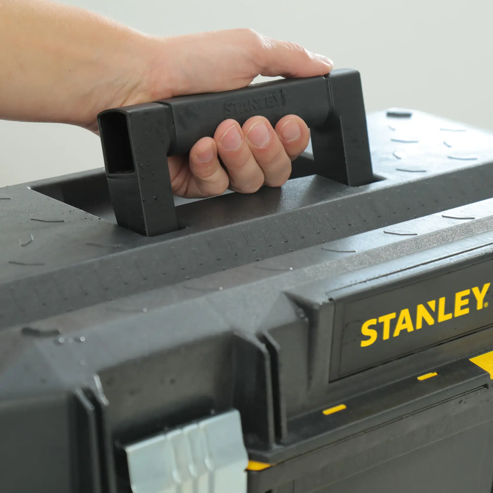 STANLEY 1-94-749 maniglia della cassetta degli attrezzi nera in primo piano, mano che tiene, logo giallo visibile.
