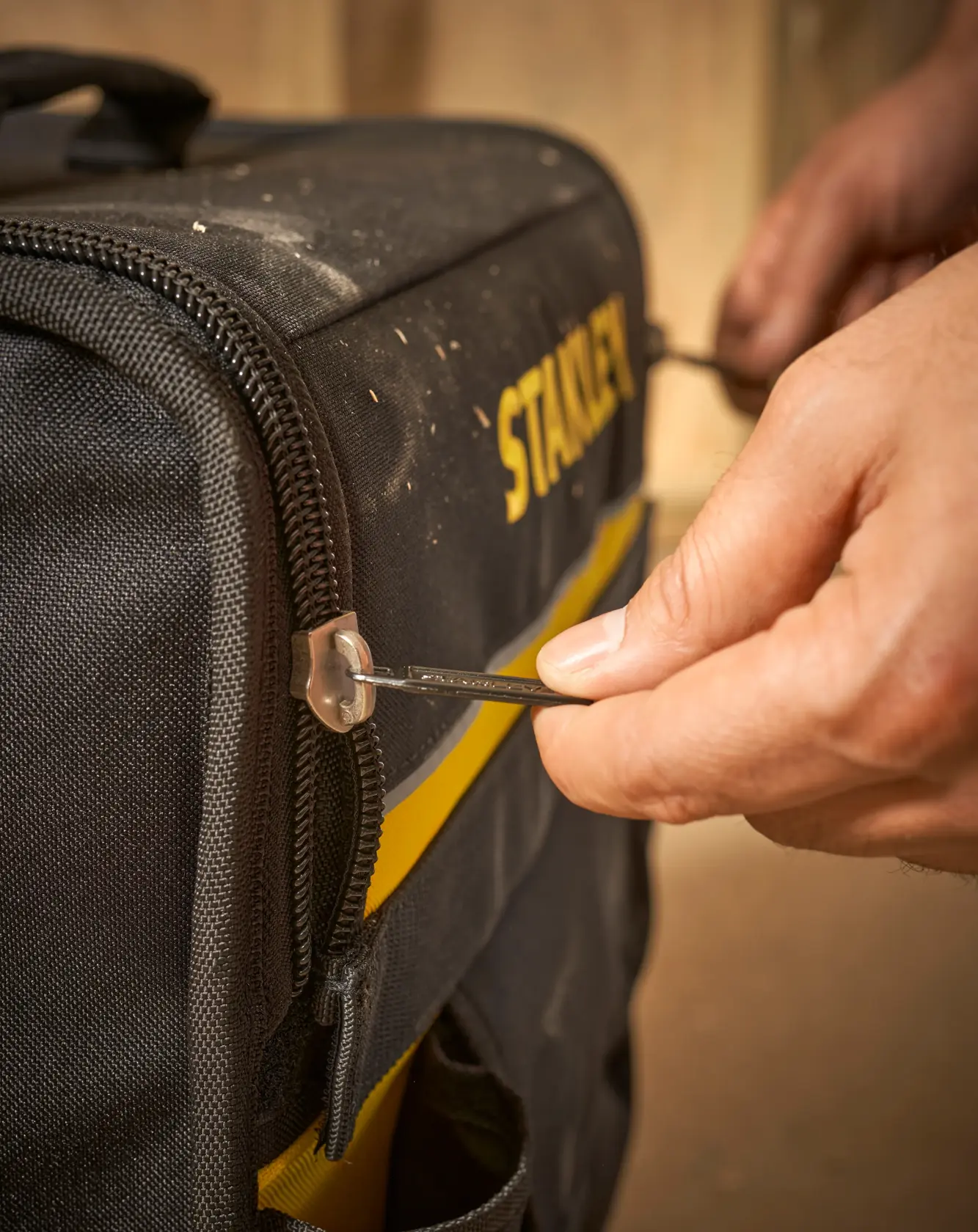 STANLEY 1-97-515 borsa per attrezzi fotografia, primo piano di mano che usa la zip su borsa nera e gialla.