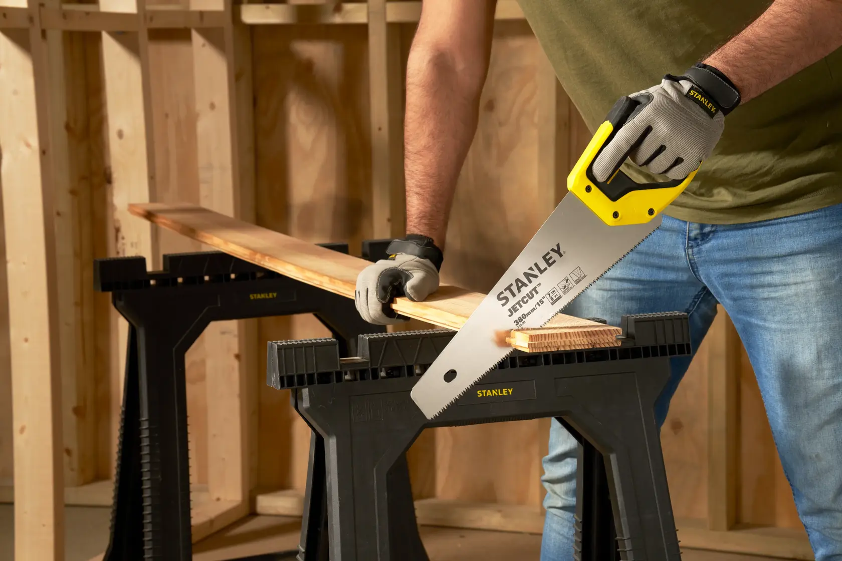 STANLEY 2-15-281 sega manuale con manico giallo taglia una tavola di legno su cavalletto nero in officina.