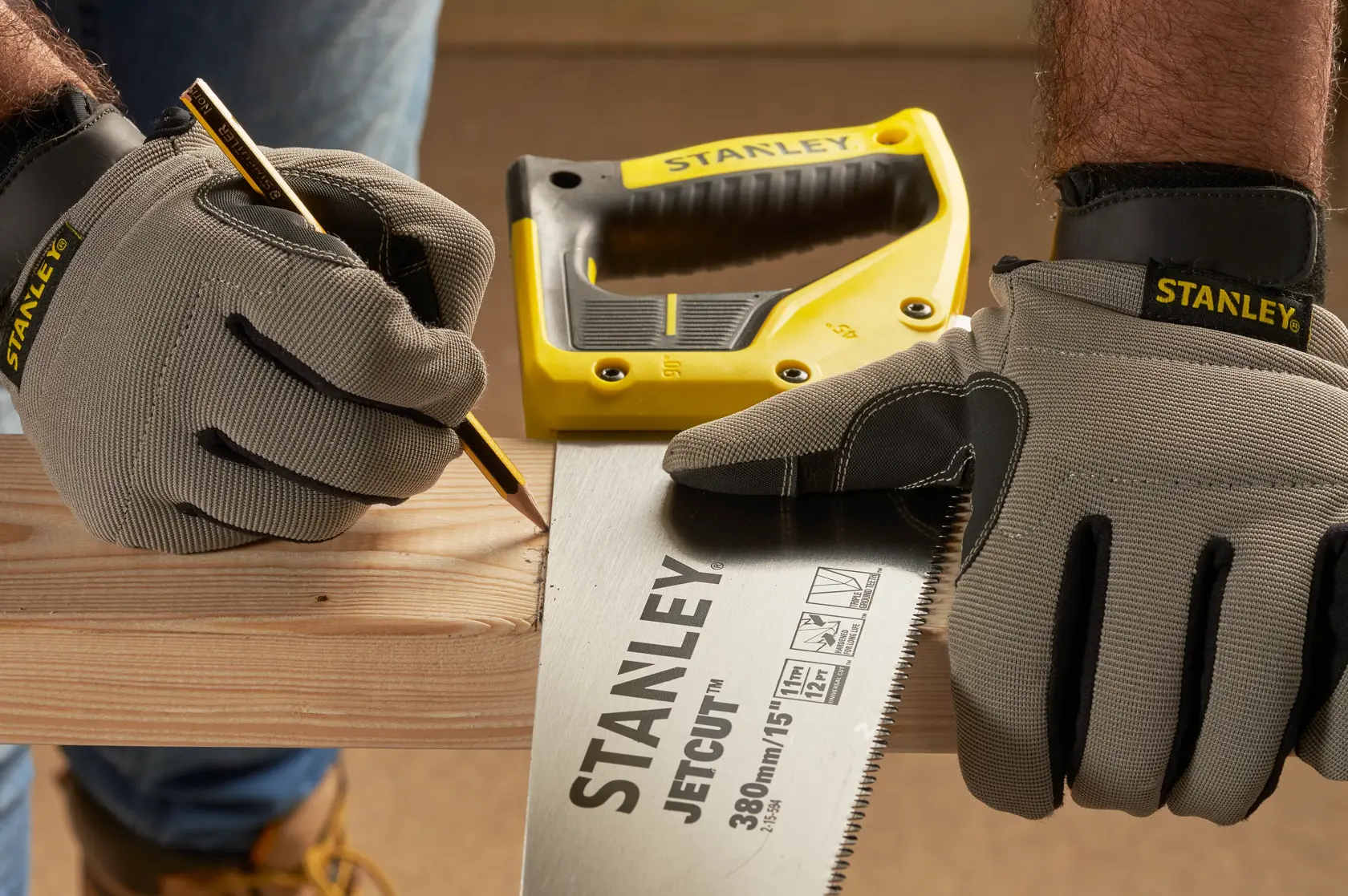 STANLEY 2-15-594 seghetto manuale in uso, mani con guanti segnano il legno, matita e manico giallo visibili.