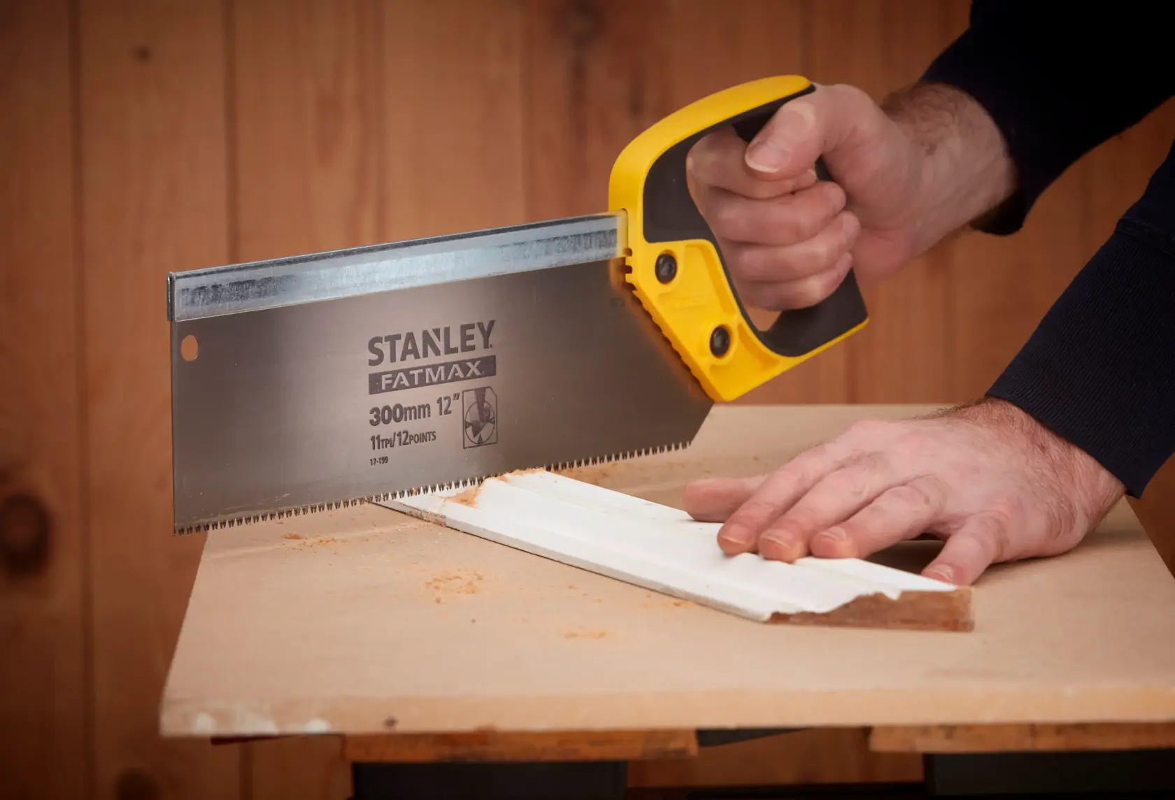 Stanley 2-17-199 seghetto manuale con manico giallo taglia una modanatura bianca su banco da lavoro, vista laterale.
