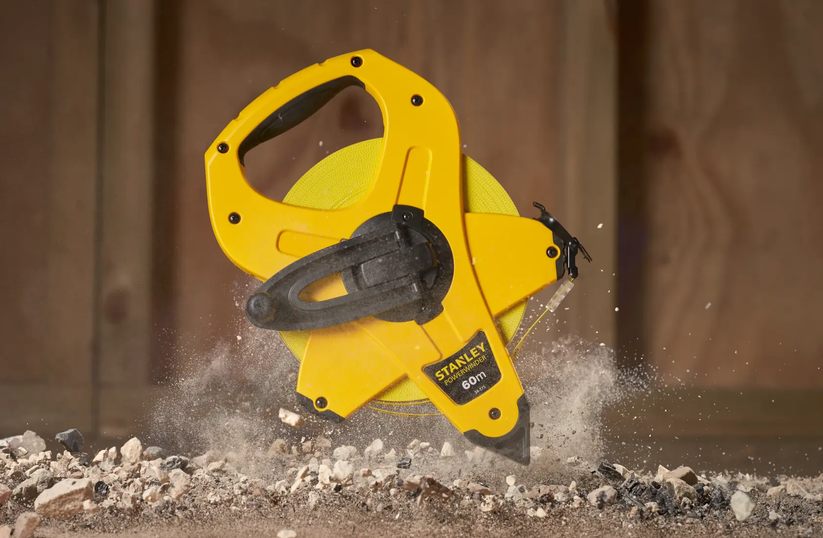 STANLEY 2-34-775 metro a nastro giallo a bobina aperta, 60m, impugnatura nera, su detriti da costruzione.