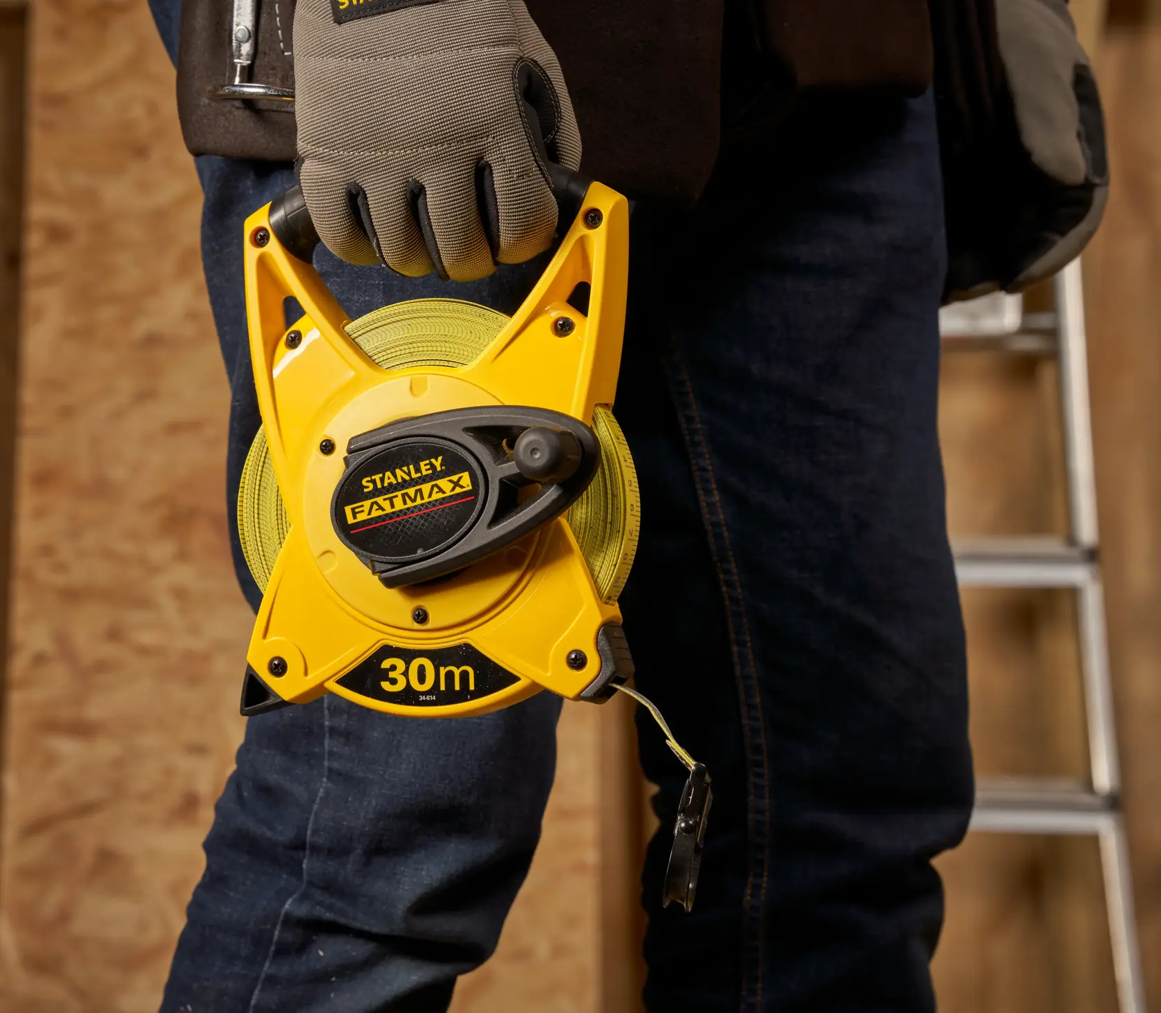 STANLEY 2-34-814 metro a nastro FATMAX aperto 30m tenuto da una mano guantata, sfondo officina.