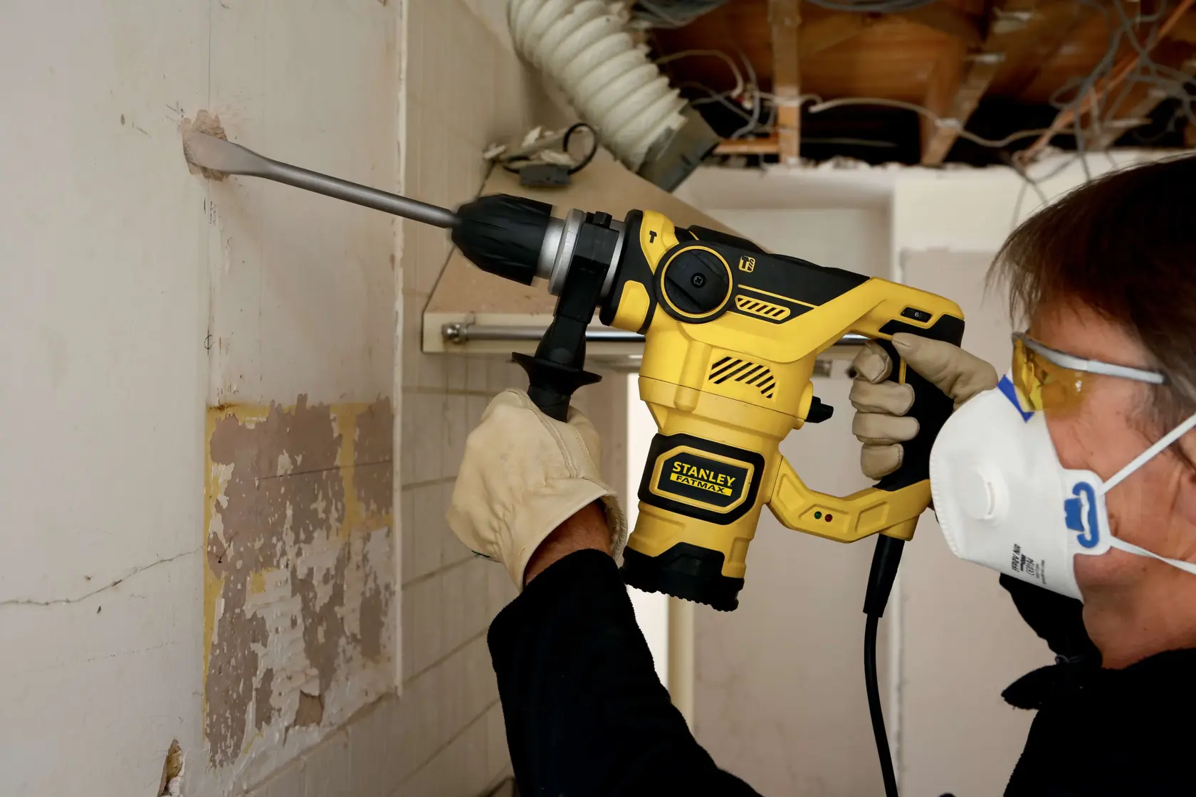 Foto di persona che usa il martello rotativo STANLEY FME1250K, perforando un muro con guanti e mascherina.