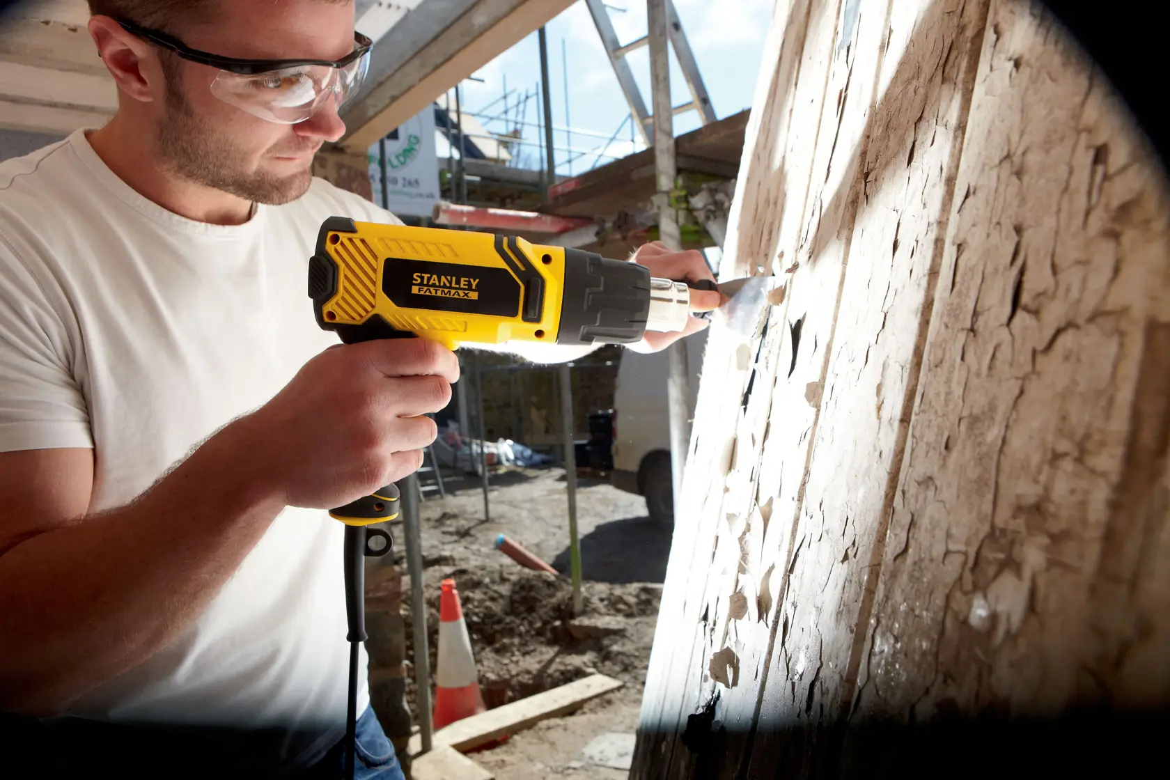 Foto della pistola termica STANLEY FME670K usata per rimuovere vernice da una superficie in legno in cantiere.