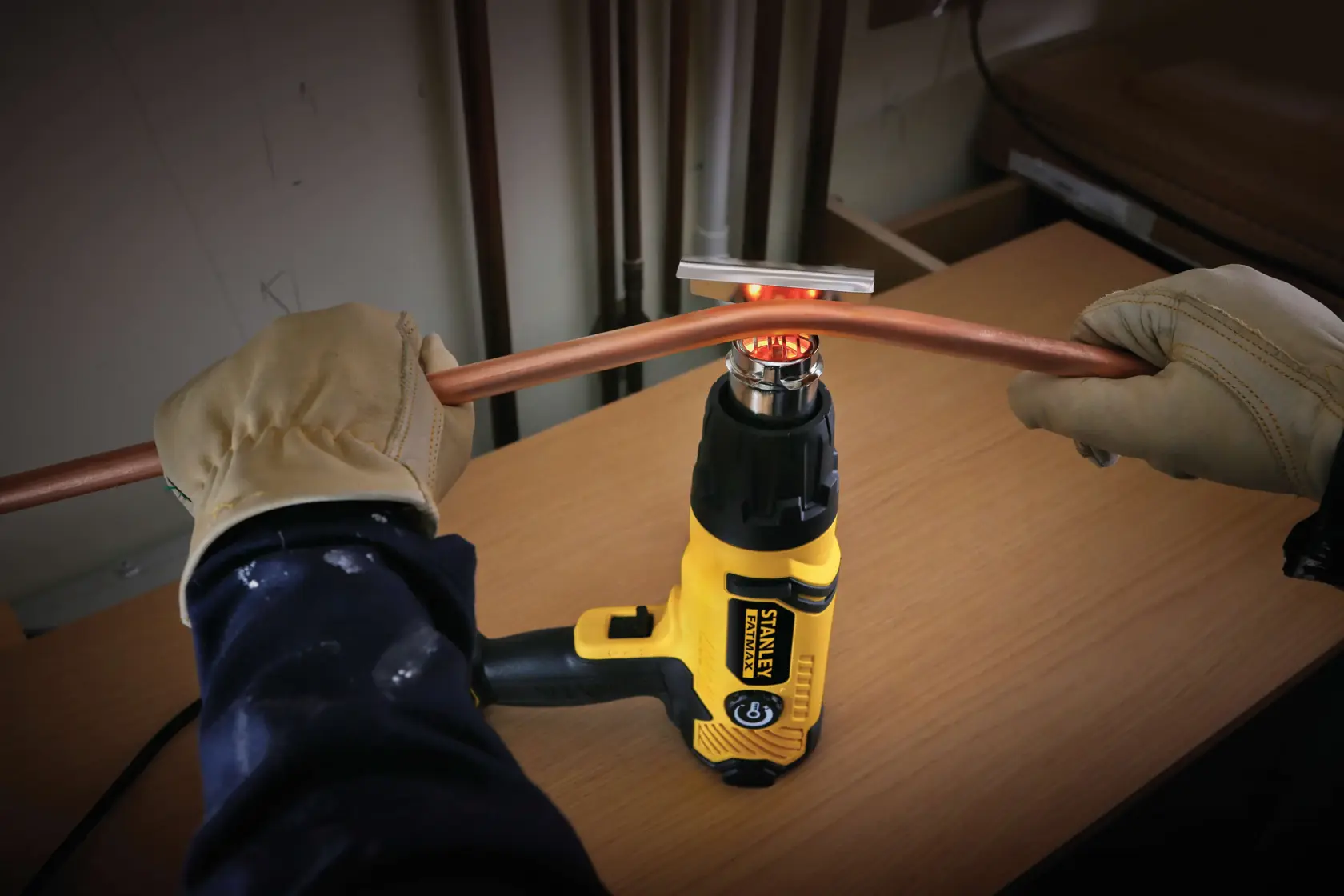 STANLEY FME670K pistola termica in uso per piegare un tubo di rame, persona con guanti regge il tubo sul banco.