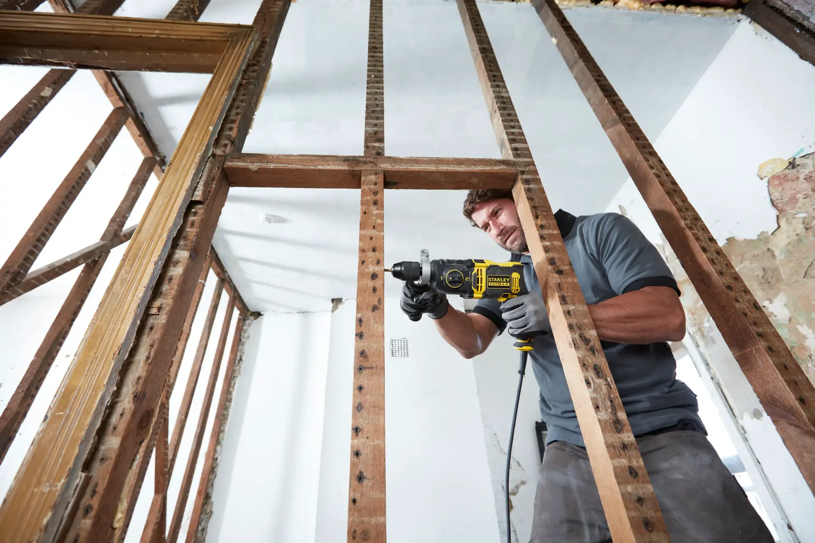 Trapano a percussione con filo STANLEY FMEH750K usato in cantiere, visto attraverso travi in legno.