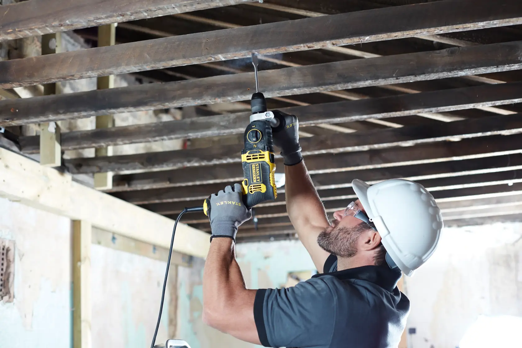 Foto di un operaio che usa il trapano a filo STANLEY FMEH850K per forare travi in legno, indossando dispositivi di sicurezza.