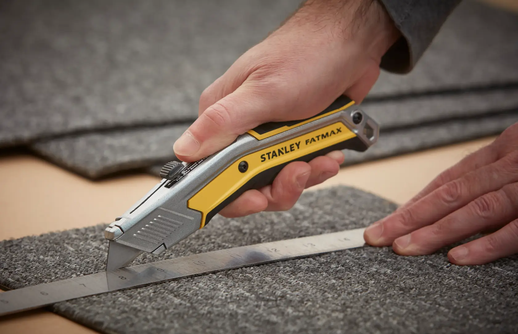 Foto del taglierino STANLEY FATMAX FMHT0-10288 che taglia un tappeto lungo un righello metallico.