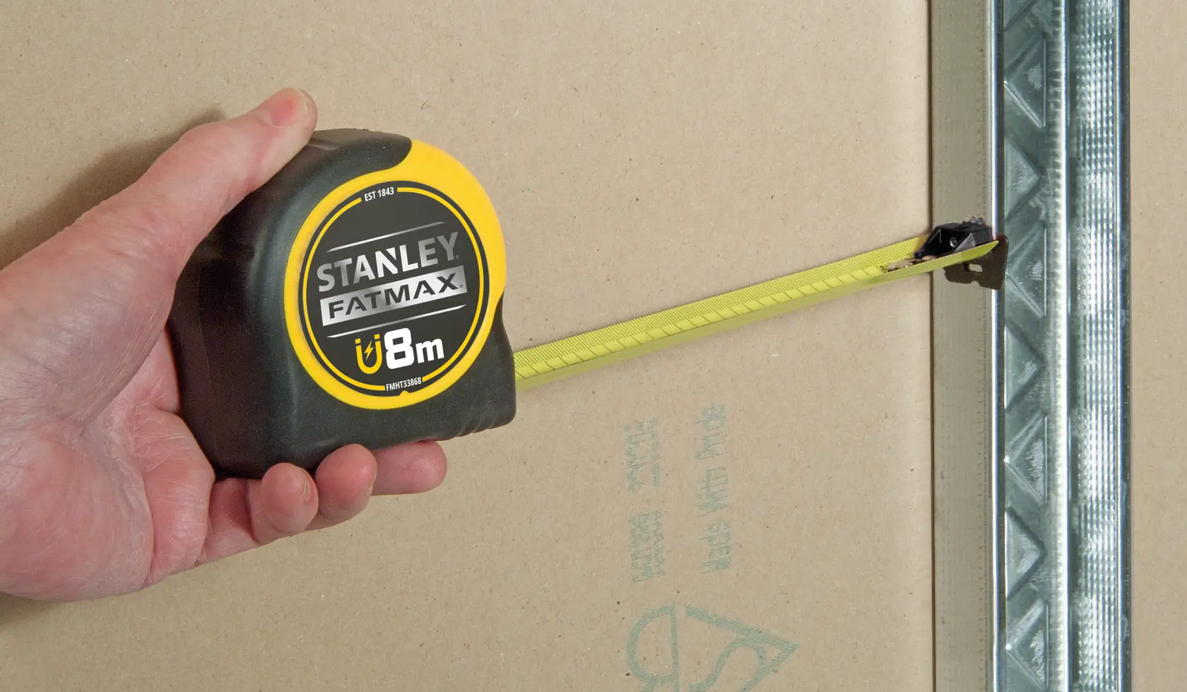 STANLEY FMHT0-33868 metro a nastro tenuto in mano, lama gialla distesa su cartongesso.
