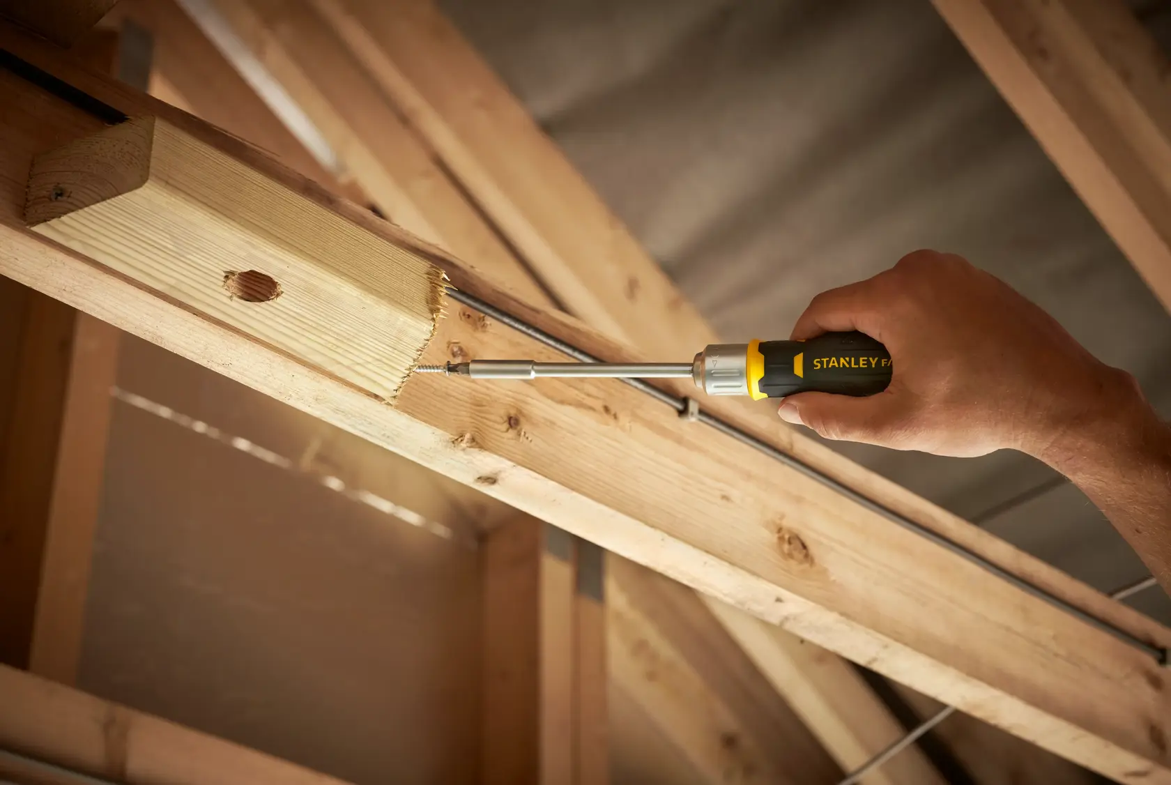 Cacciavite Stanley FMHT0-62690 avvita una vite in una trave di legno, primo piano in cantiere.
