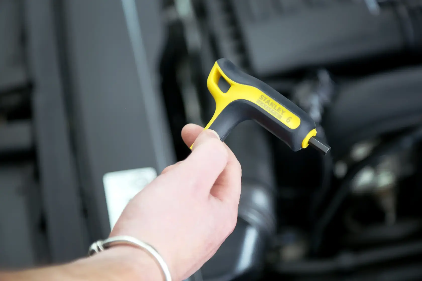 Stanley FMHT0-69049 chiave esagonale con manico giallo e nero tenuta vicino al vano motore.