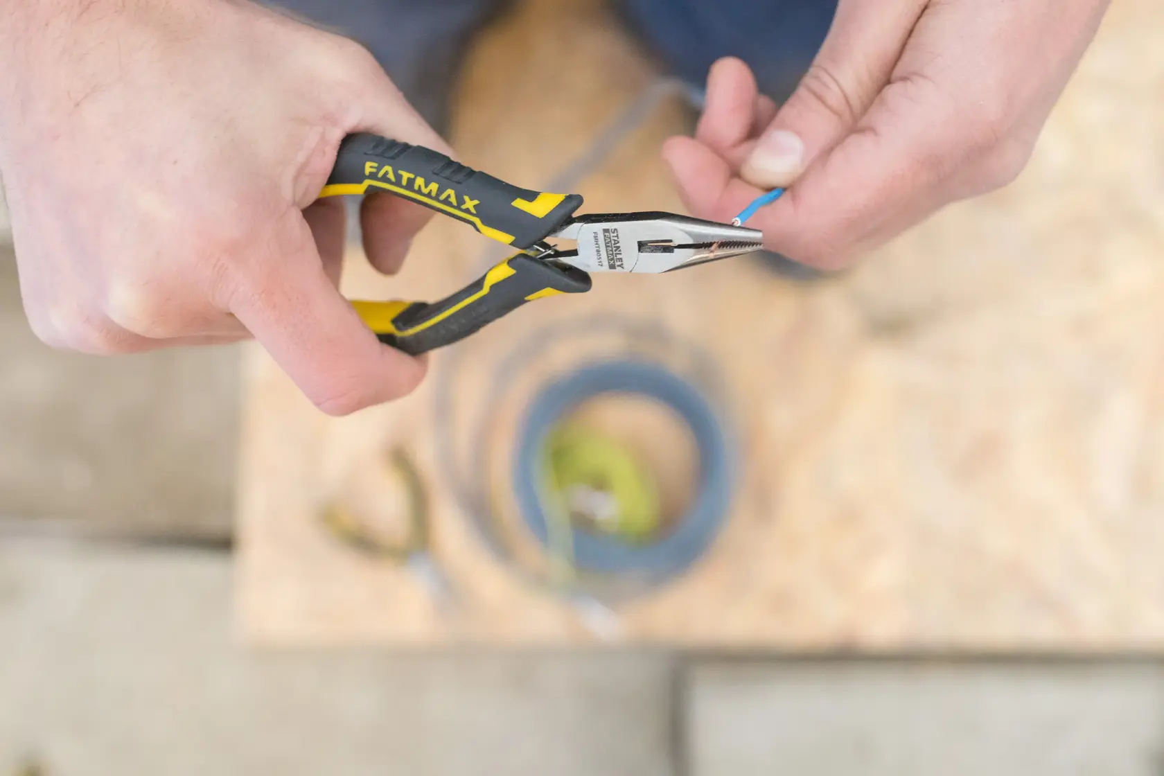 Pinza a becchi lunghi STANLEY FMHT0-80517 con manico giallo-nero, utilizzata per afferrare un filo blu.