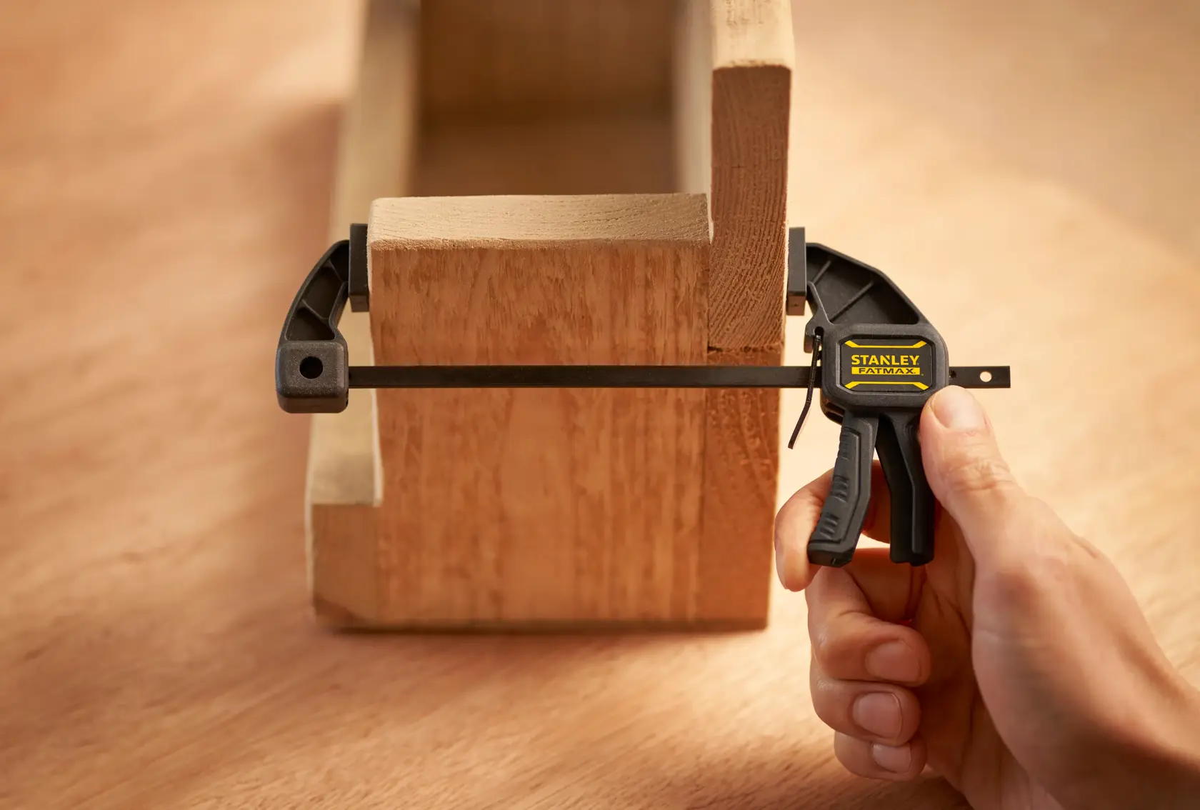 Foto del morsetto rapido STANLEY FMHT0-83231 che stringe due pezzi di legno, mano che aziona il morsetto in primo piano.