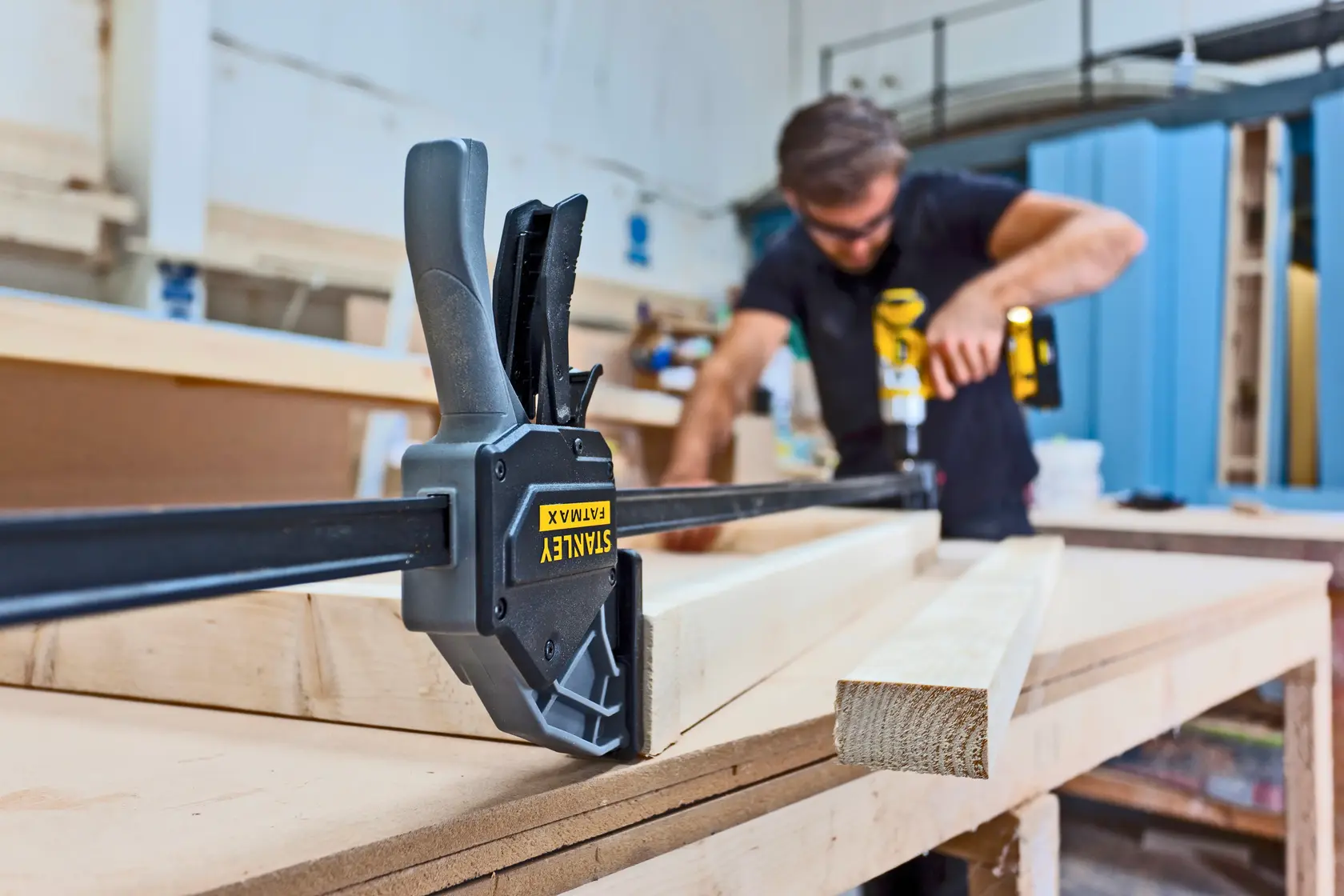 Morsetto STANLEY FMHT0-83240 che blocca legno su banco da lavoro con persona sullo sfondo.