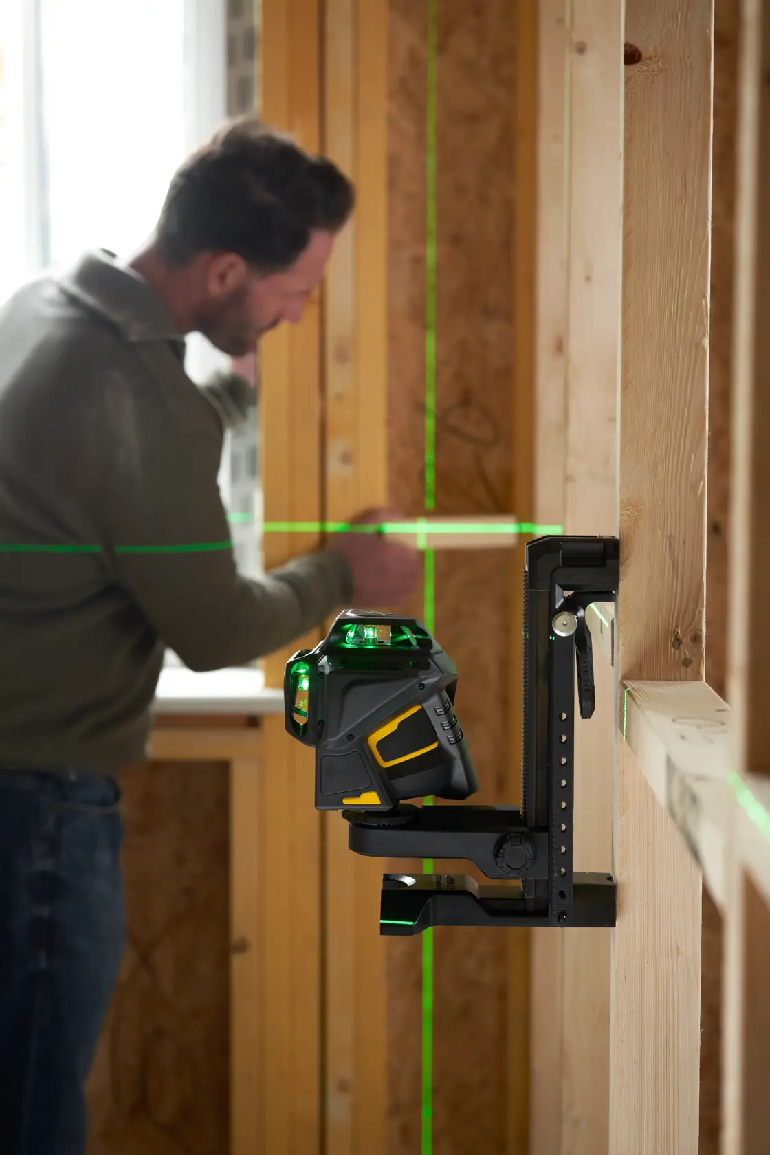 Livella laser a raggio verde STANLEY FMHT1-77356 montata a parete in cantiere, uomo sullo sfondo.