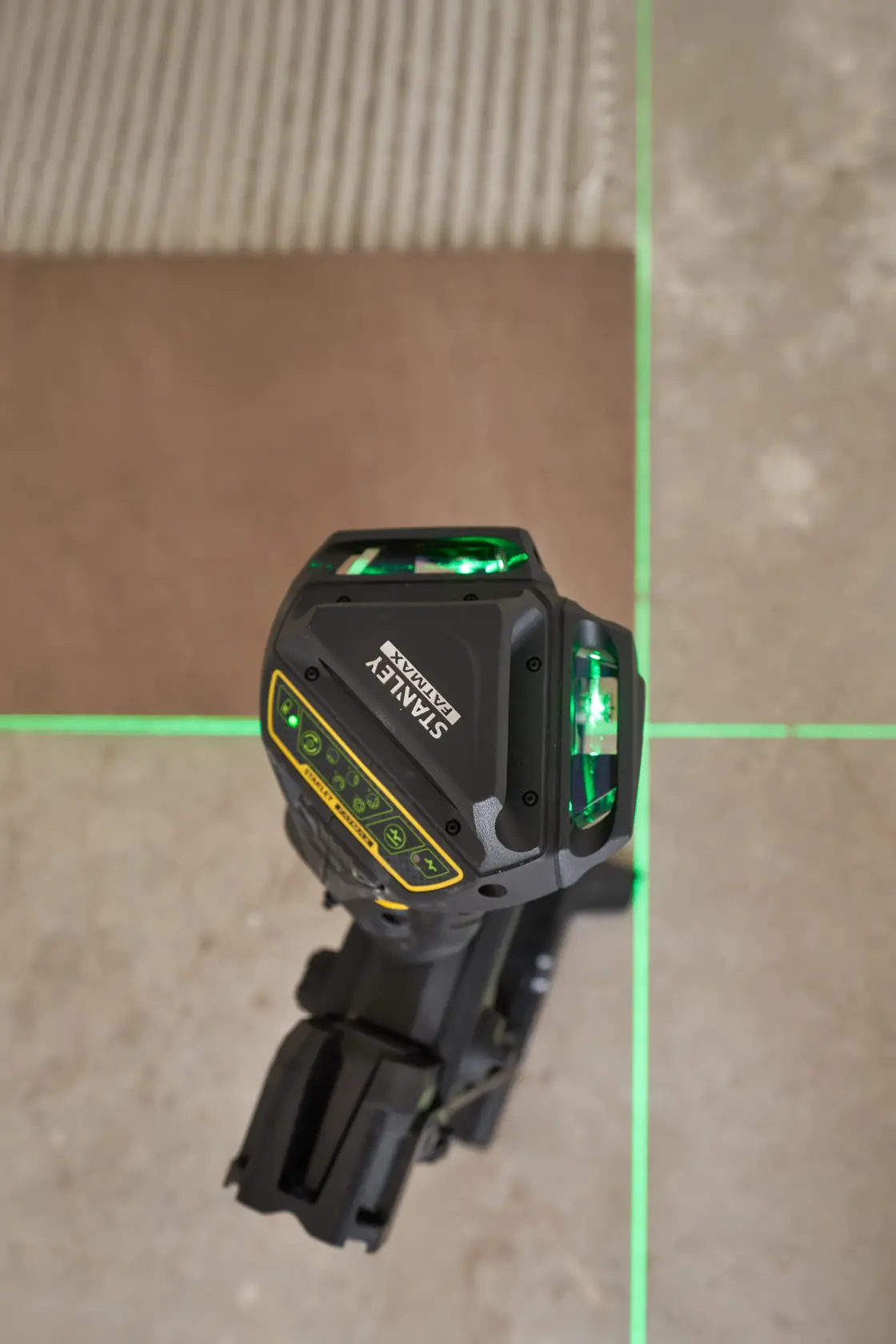 STANLEY FMHT1-77356 livello laser che proietta linee verdi luminose su un pavimento piastrellato, vista dall’alto.
