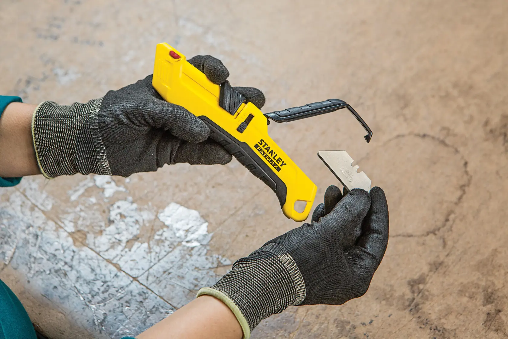 Foto del coltello multiuso STANLEY FMHT10365-0 con manico giallo e lama sostituita da mani con guanti.