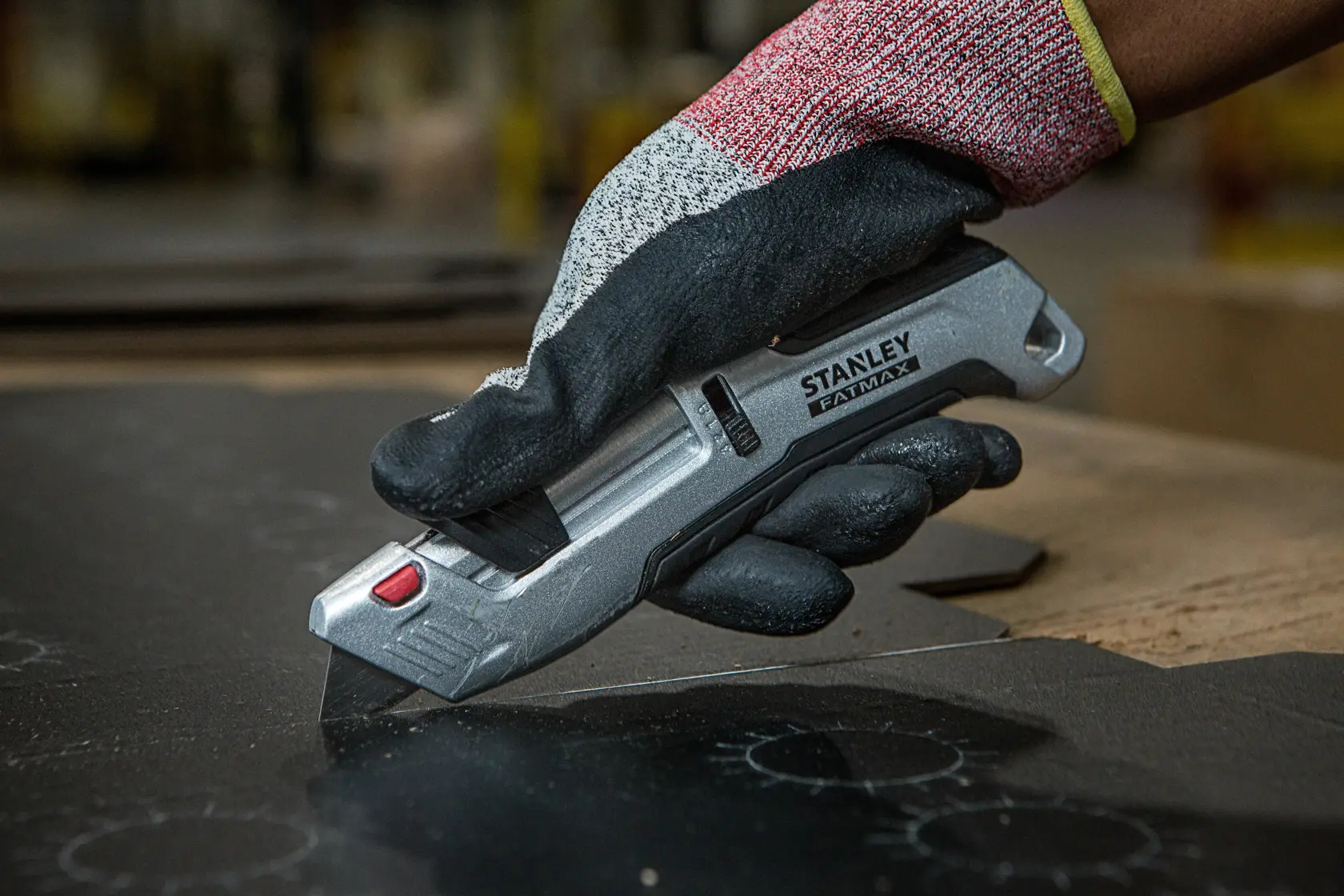 Foto del cutter STANLEY FMHT10367-0 in mano guantata che taglia materiale nero.