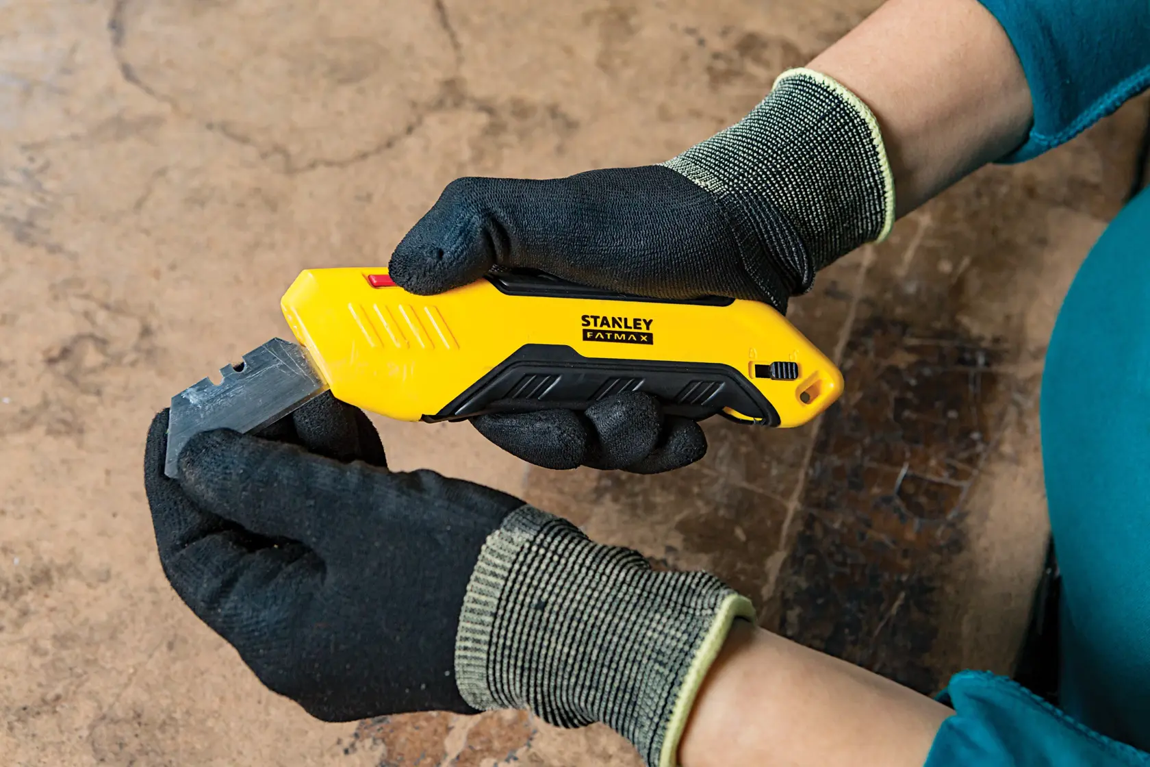 Stanley FMHT10369-0 coltello multiuso con manico giallo e nero, tenuto da mani con guanti, vista laterale.