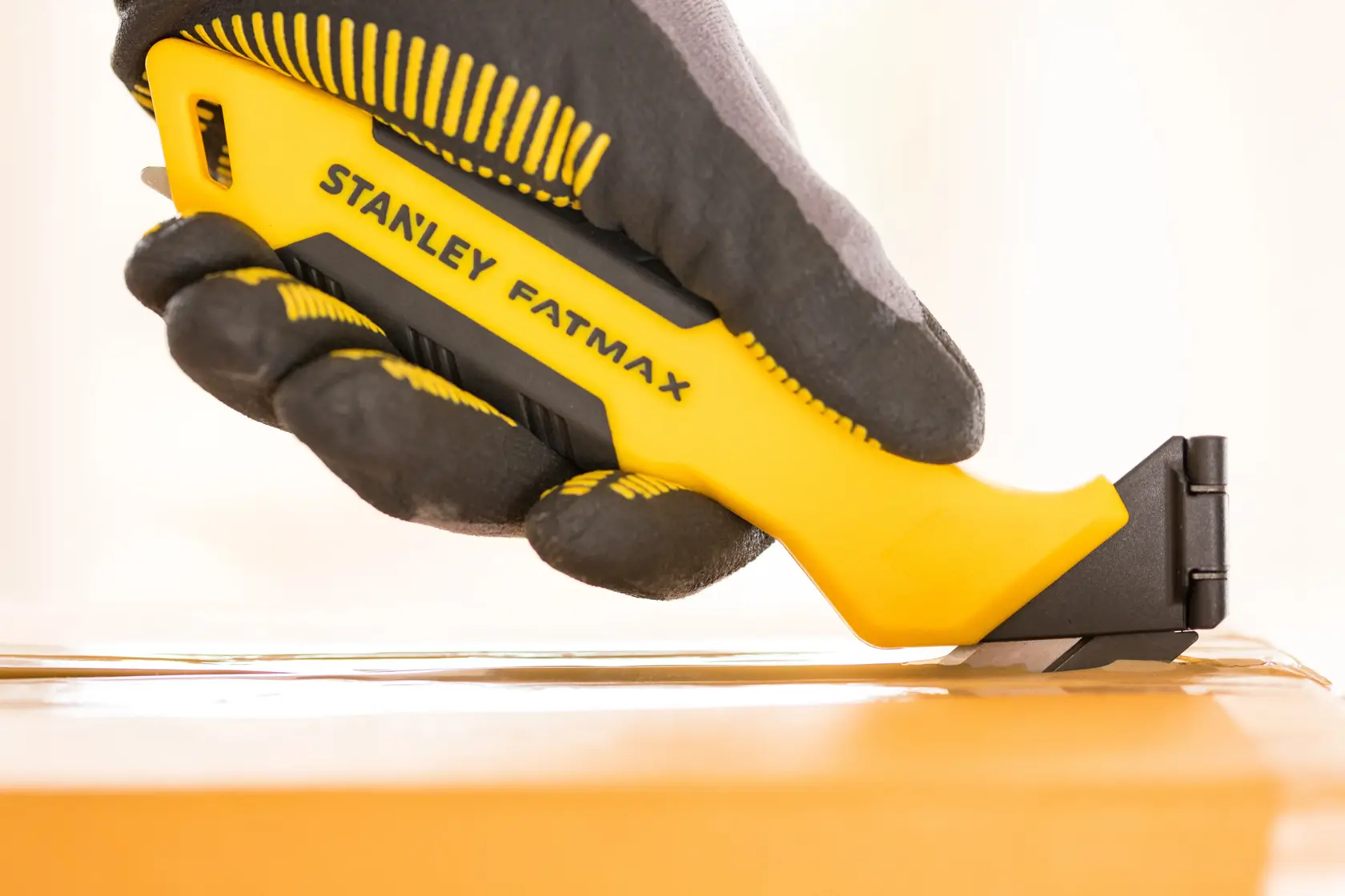 Foto del coltello universale STANLEY FMHT10373-0 in una mano con guanto, che taglia nastro su una scatola di cartone.