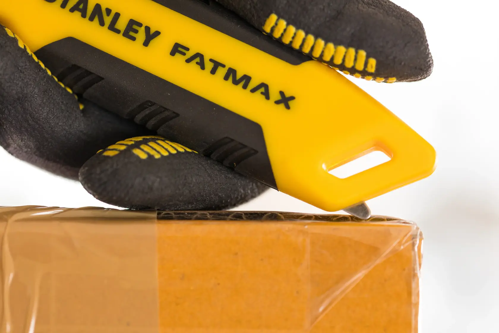 Taglierino STANLEY FMHT10373-0 con manico giallo e nero, che taglia nastro su scatola di cartone, primo piano.
